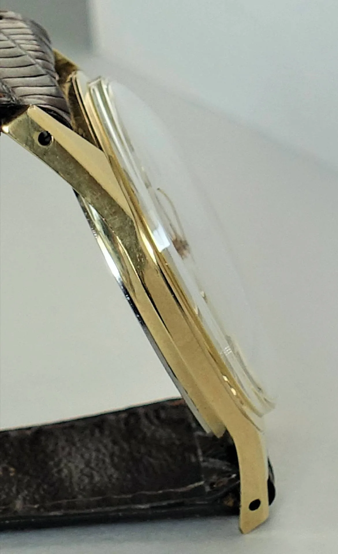 Armbanduhr goldfarben Seitliche Ansicht einer goldfarbenen Armbanduhr mit braunem Armband und gewölbtem Uhrglas.