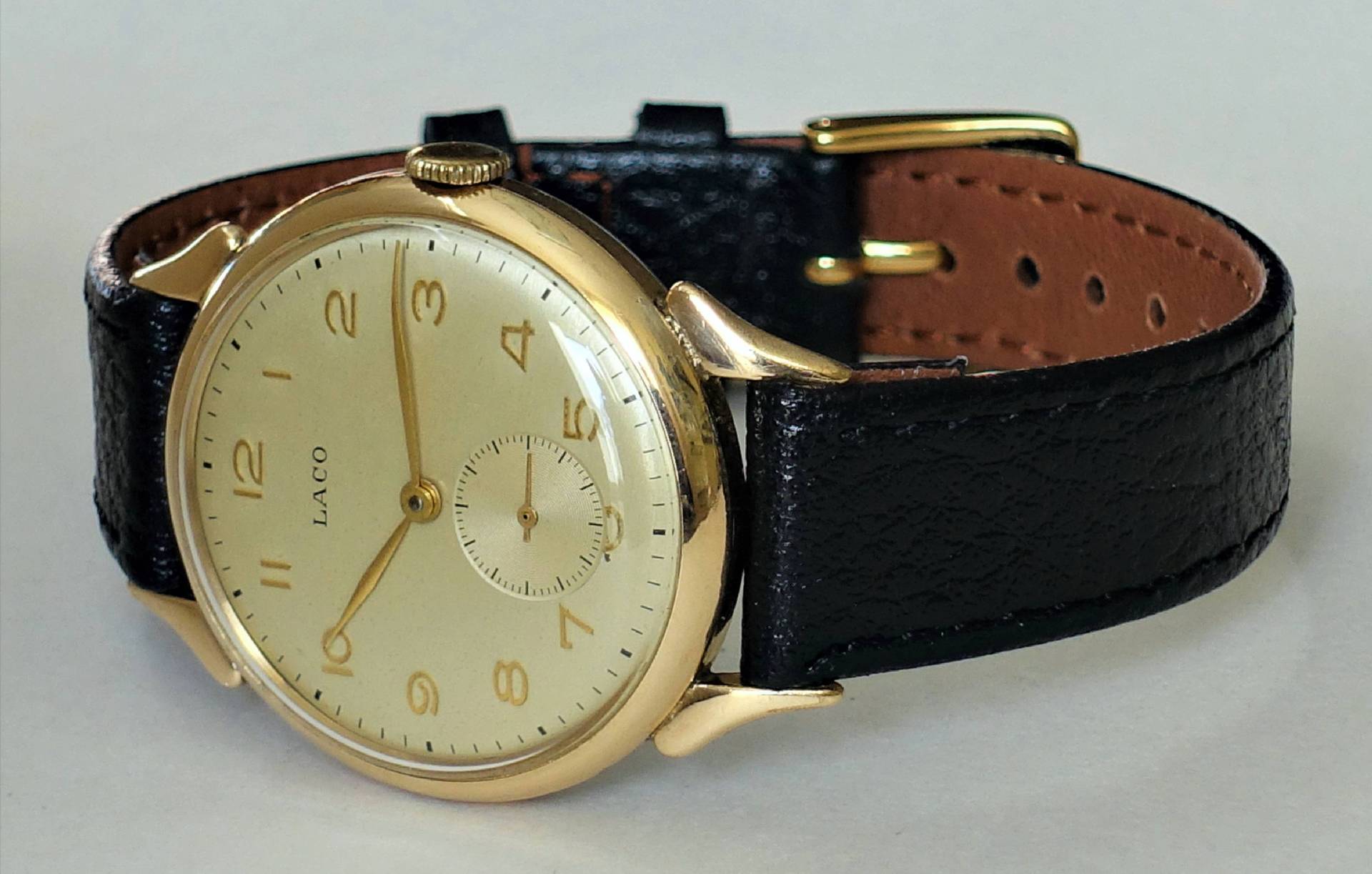 Goldfarbene Armbanduhr mit hellem Zifferblatt und schwarzem Lederarmband.