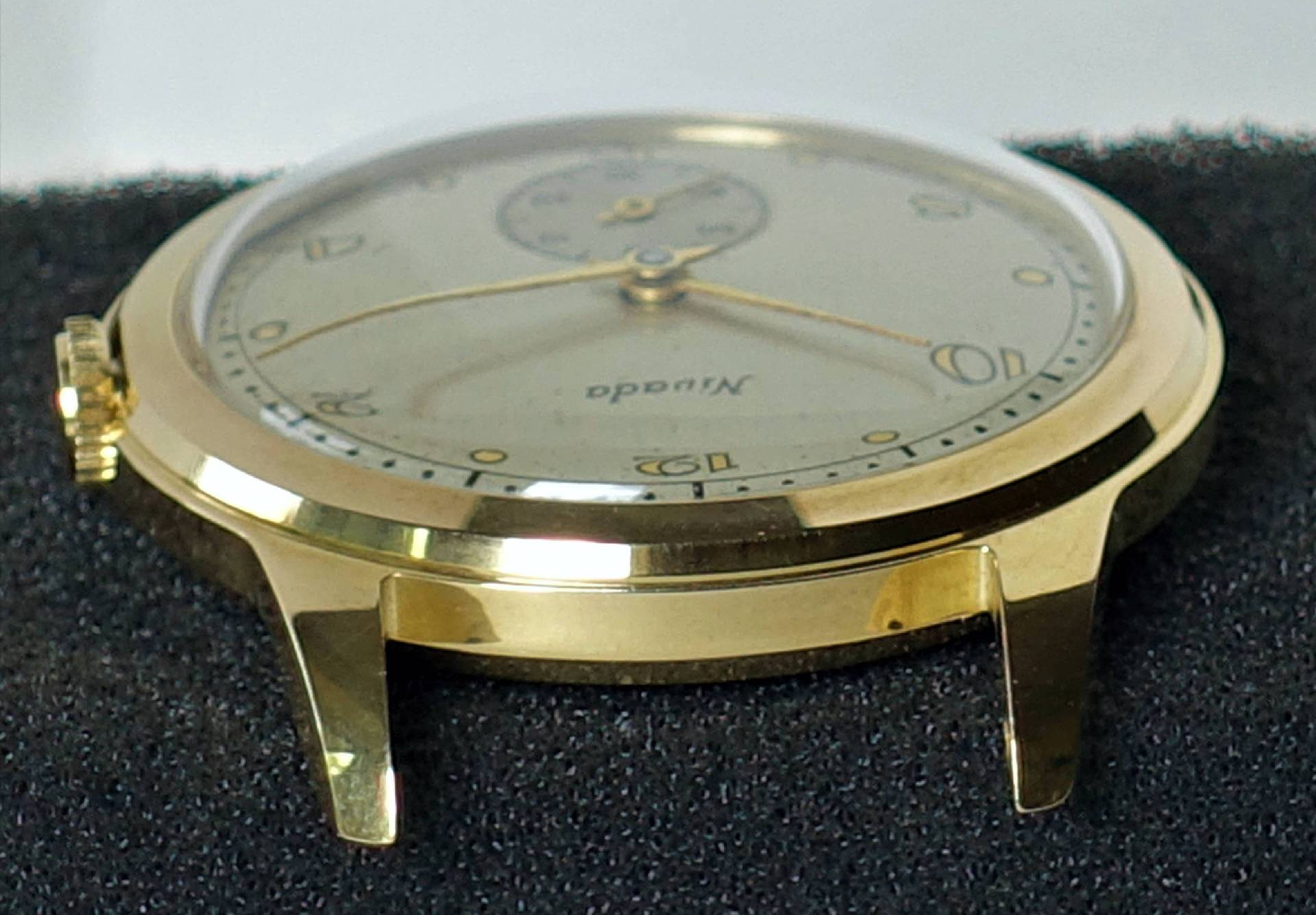 Flache Armbanduhr mit goldfarbenem Gehäuse und hellem Zifferblatt.