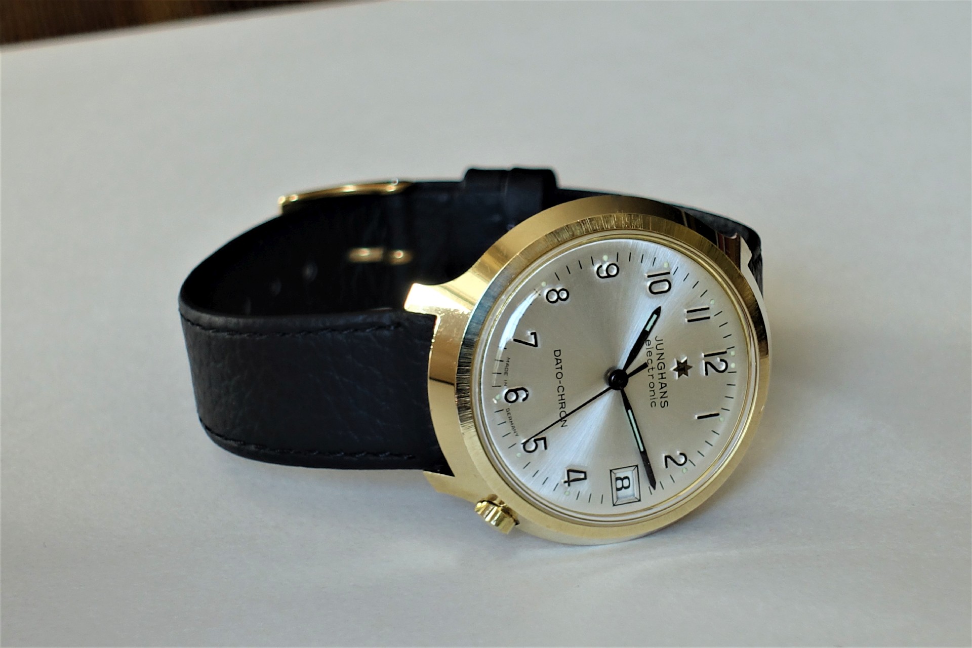 Analoge Armbanduhr mit goldfarbenem Gehäuse, silberfarbenem Zifferblatt und schwarzem Armband.