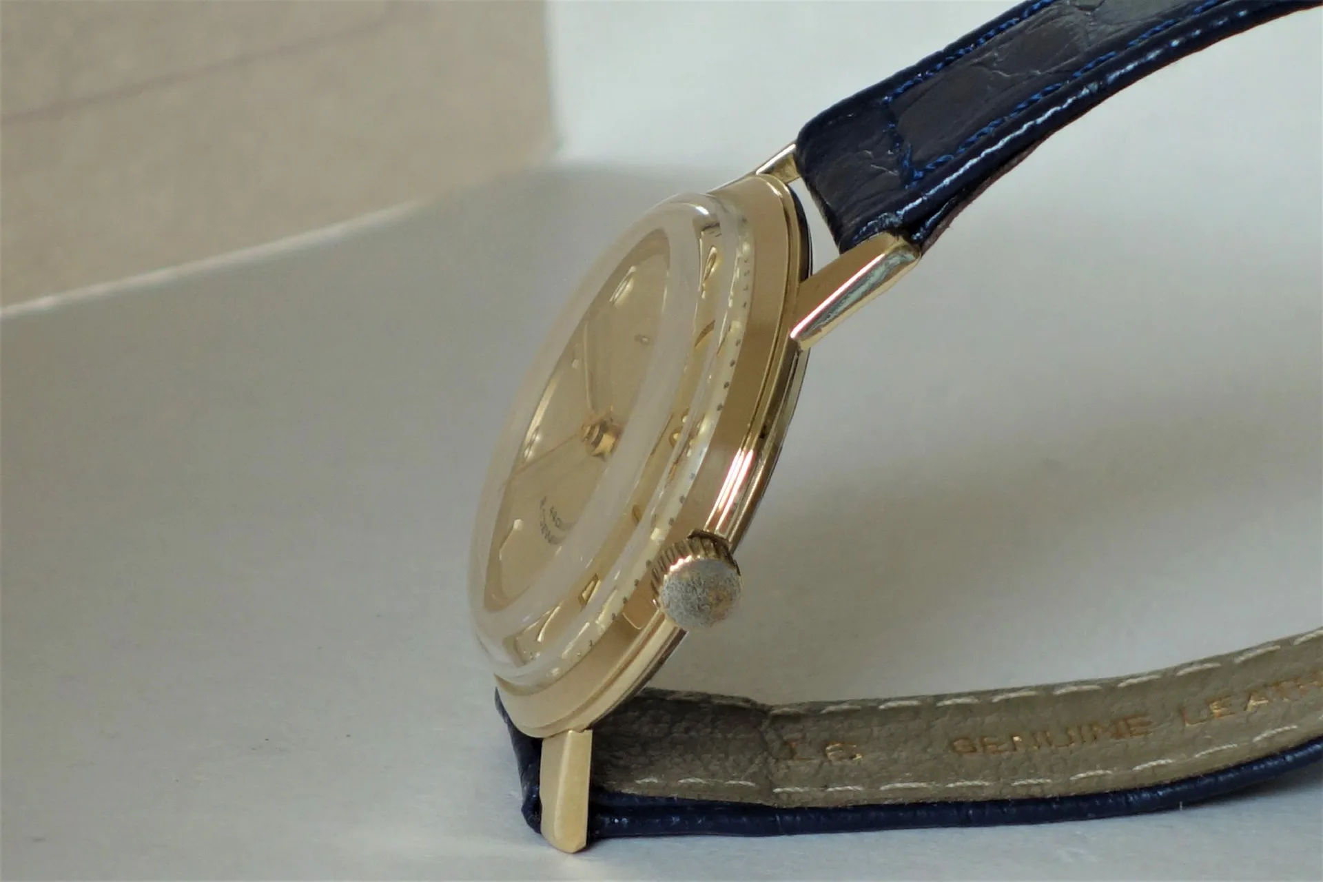 Flache Armbanduhr mit hellem Gehäuse und blauem Lederarmband.