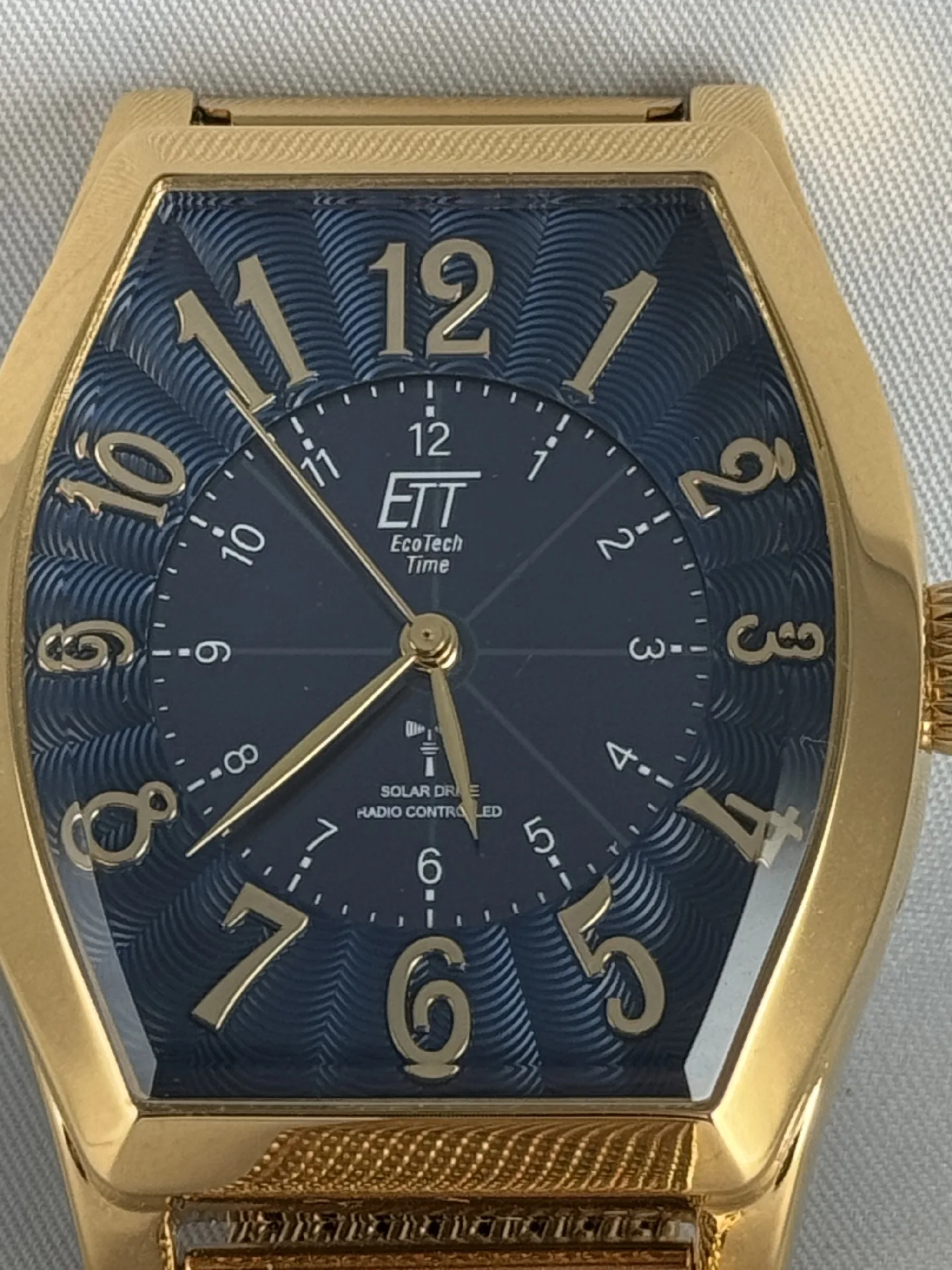 Goldfarbene Armbanduhr mit blauem Zifferblatt und arabischen Zahlen, rechteckiges Gehäuse.
