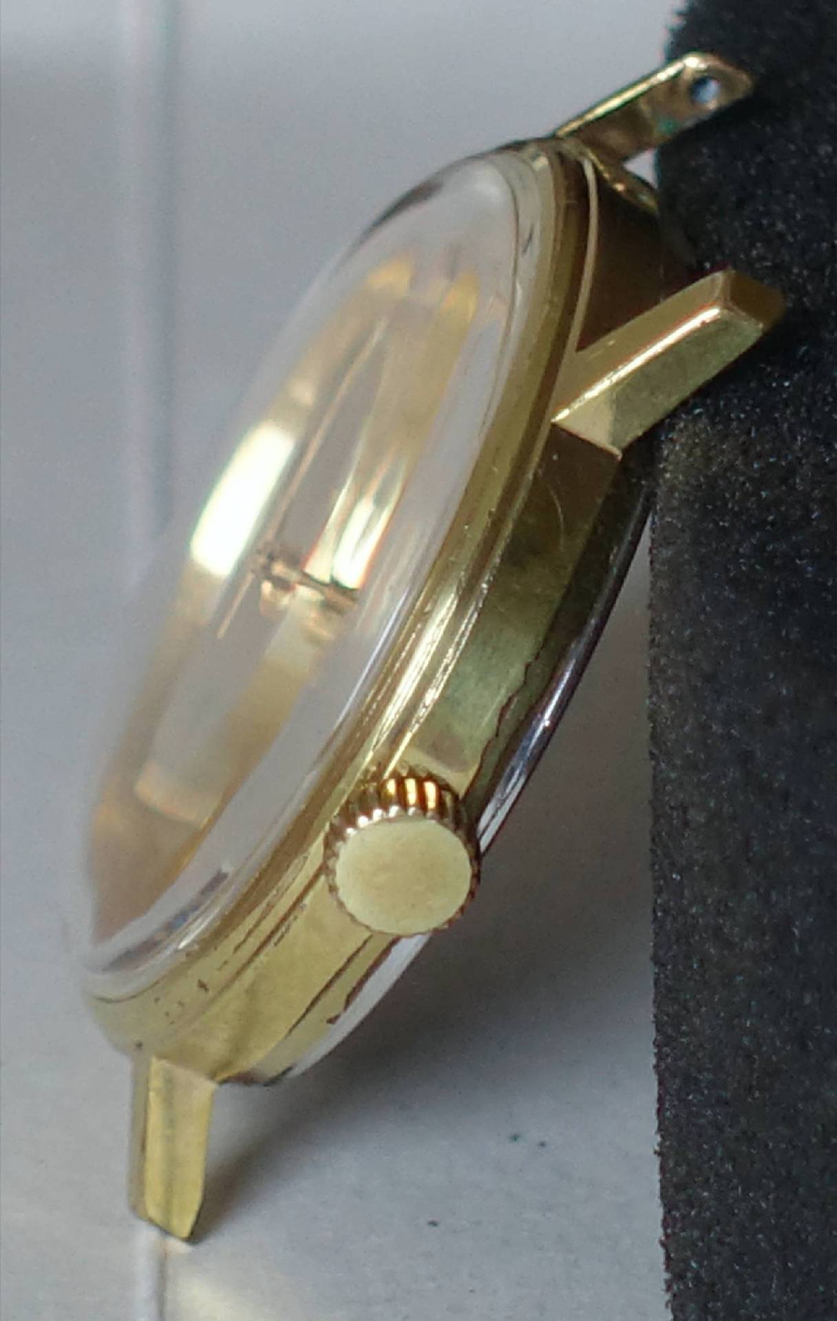 Goldfarbenes Uhrengehäuse mit seitlicher Krone und gewölbtem Glas.