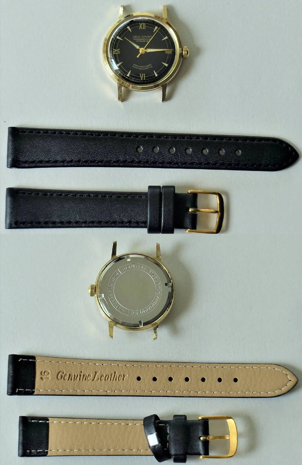 Armbanduhr goldfarben schwarz Zerlegte Armbanduhr mit goldfarbenem Gehäuse, schwarzem Zifferblatt und zwei schwarzen Lederarmbändern mit goldfarbener Schließe.