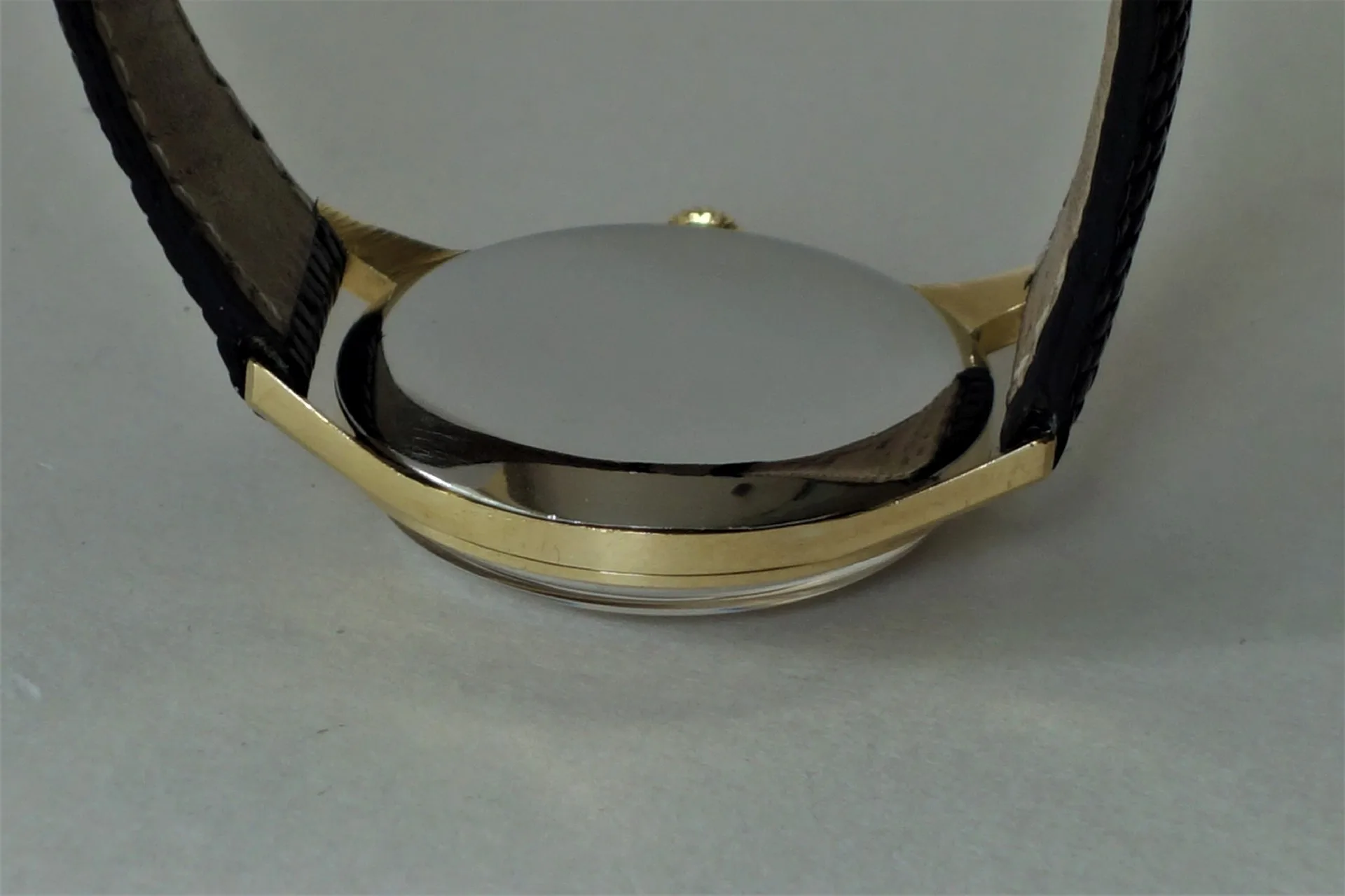 Uhrenboden silberfarben Silberfarbener Uhrenboden an einem Gehäuse mit goldfarbener Umrandung und schwarzem Armband.