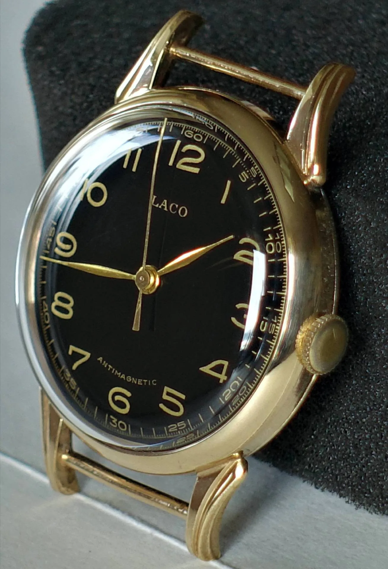 Eine Armbanduhr mit goldfarbenem Gehäuse und schwarzen Zifferblatt mit goldenen Zahlen und Zeigern, ohne montiertes Armband.