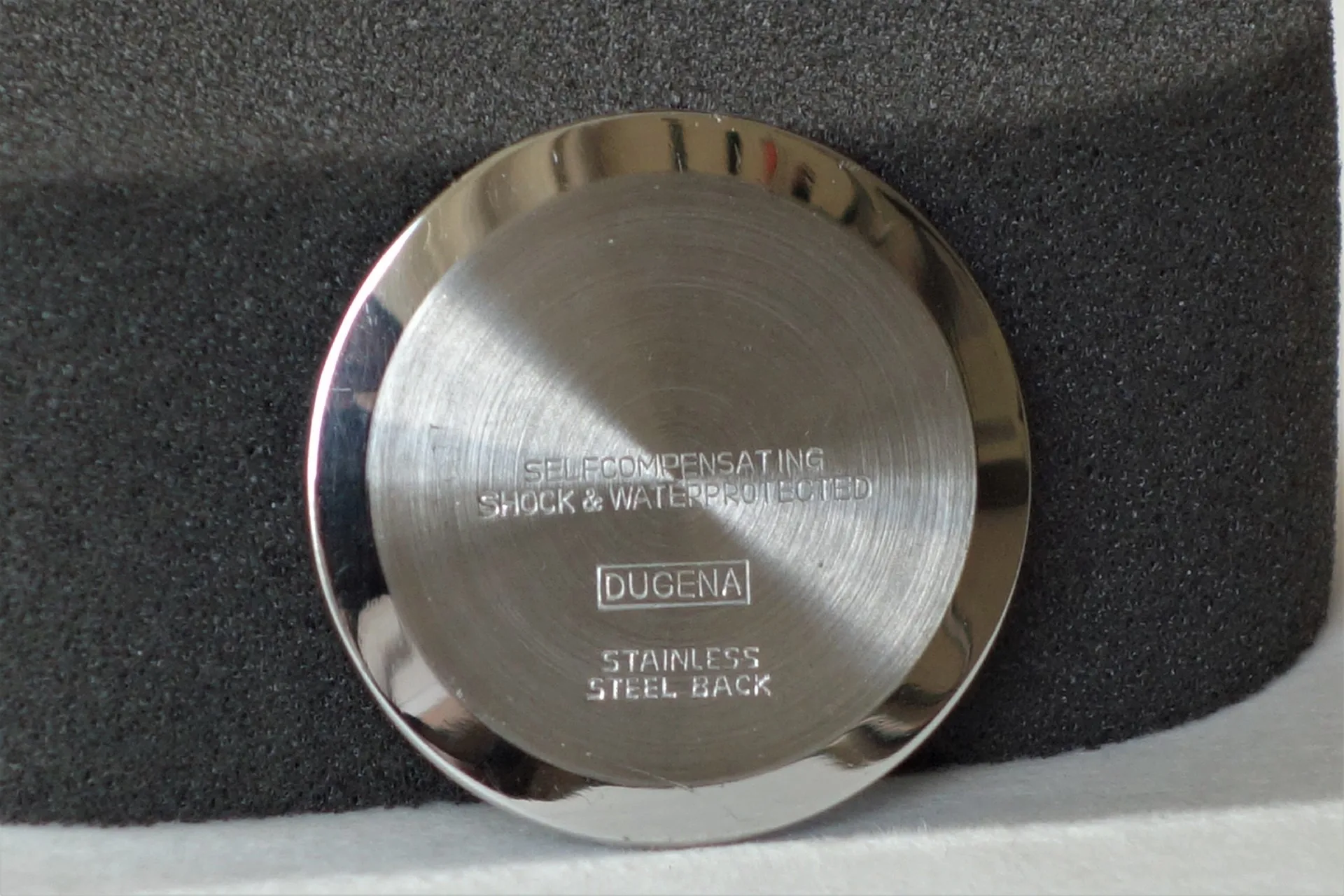 Silberfarbener Uhrenboden mit Dugena-Logo und Gravur.