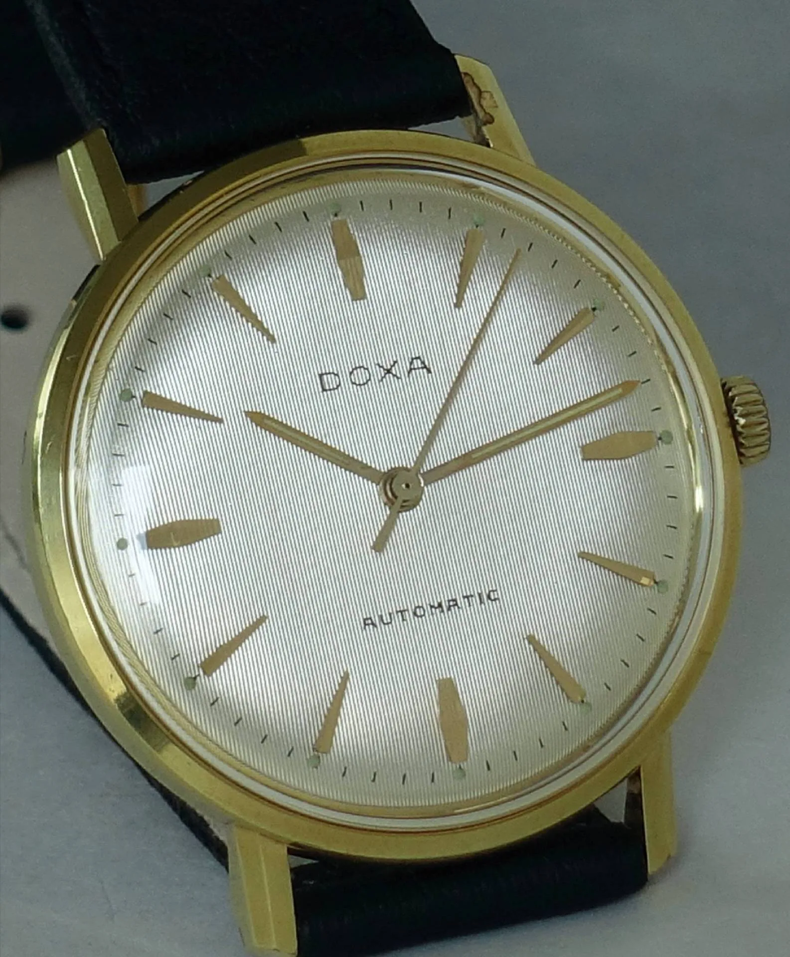 Goldfarbene Doxa Armbanduhr mit hellem Zifferblatt und schwarzem Armband.