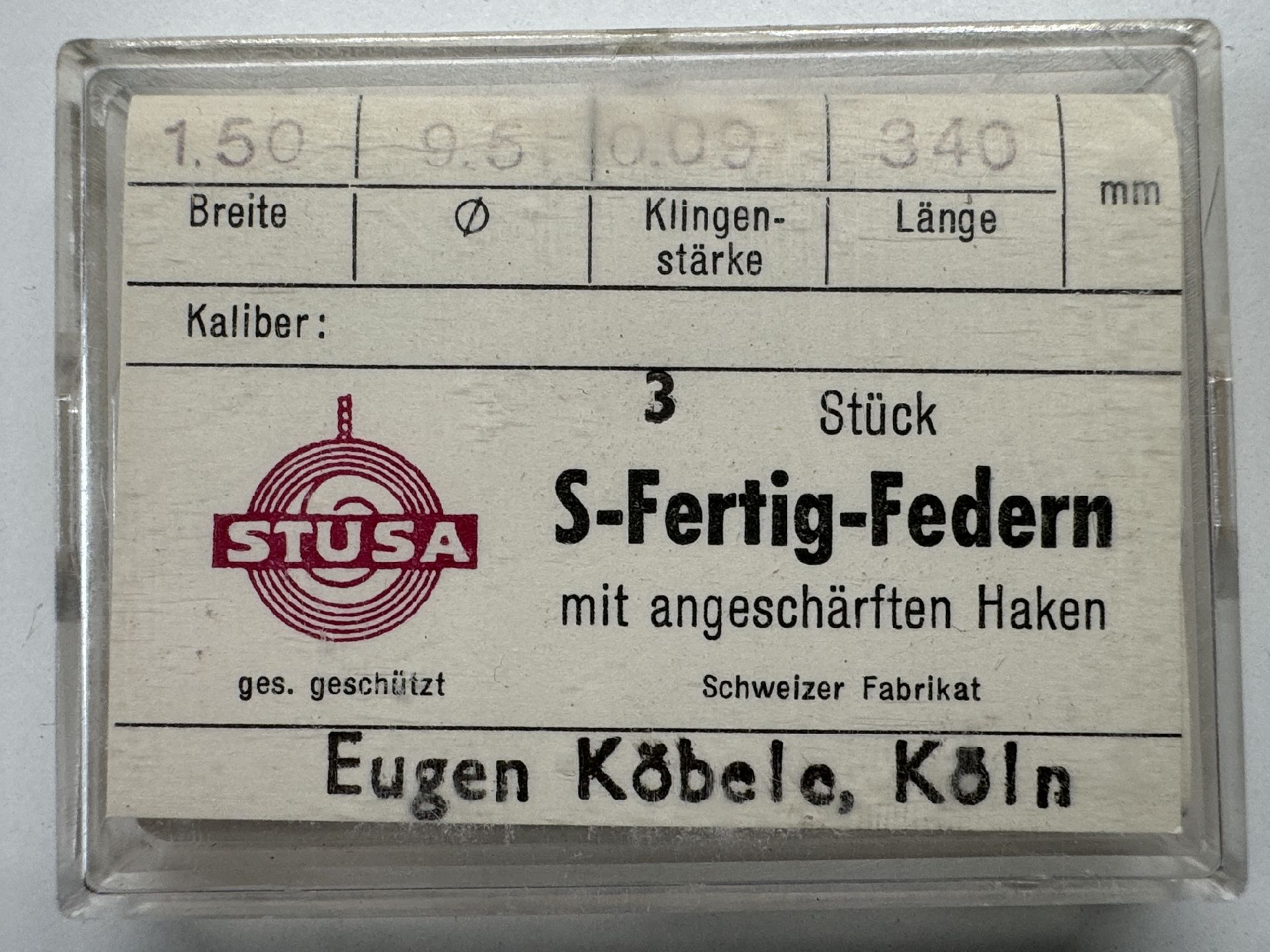 Verpackung mit drei Uhrmacher-Federn mit angeschärften Haken in transparenter Box.
