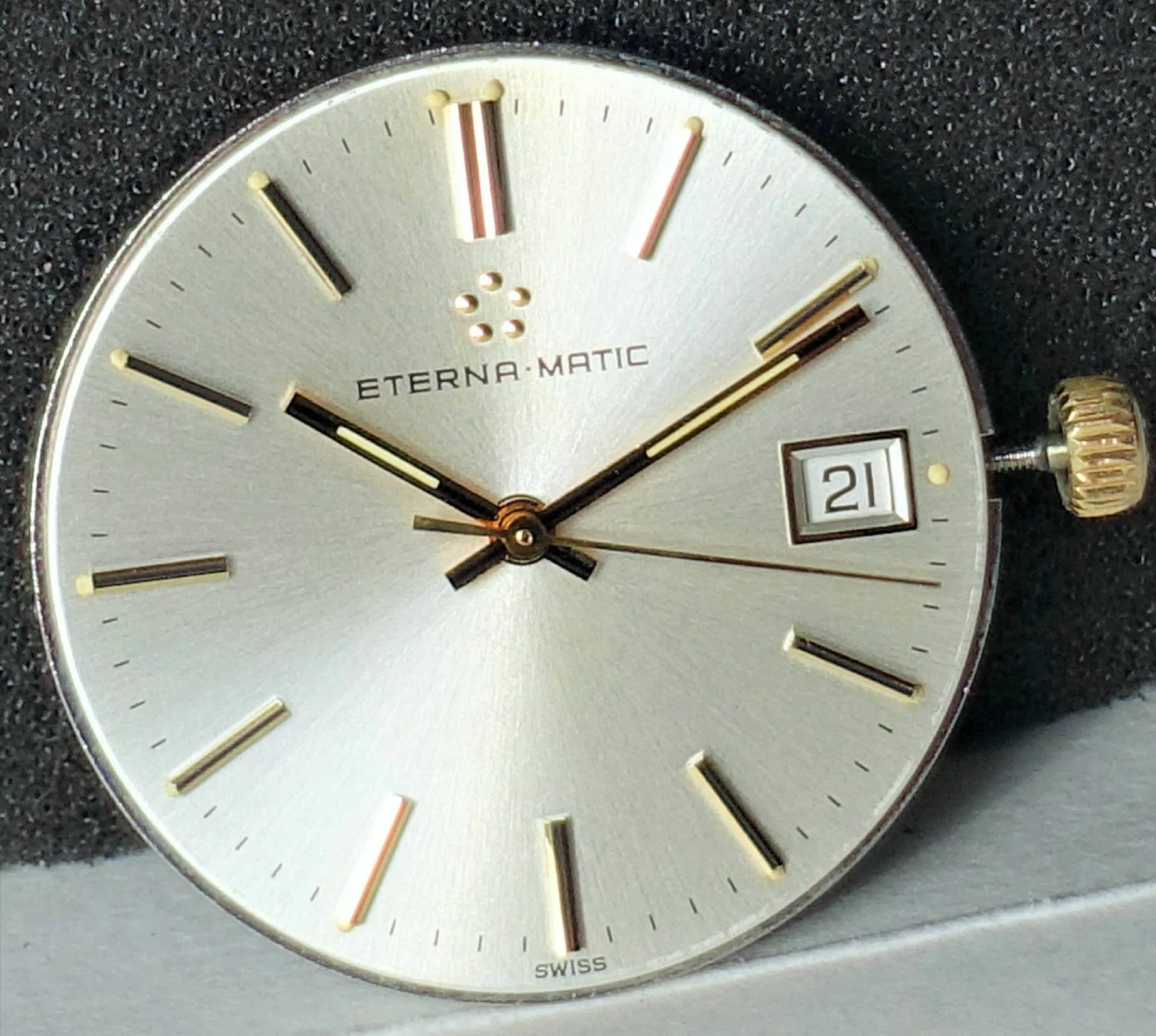 Silberfarbenes Uhrwerk mit Zifferblatt, goldfarbenen Zeigern und Datumsanzeige.