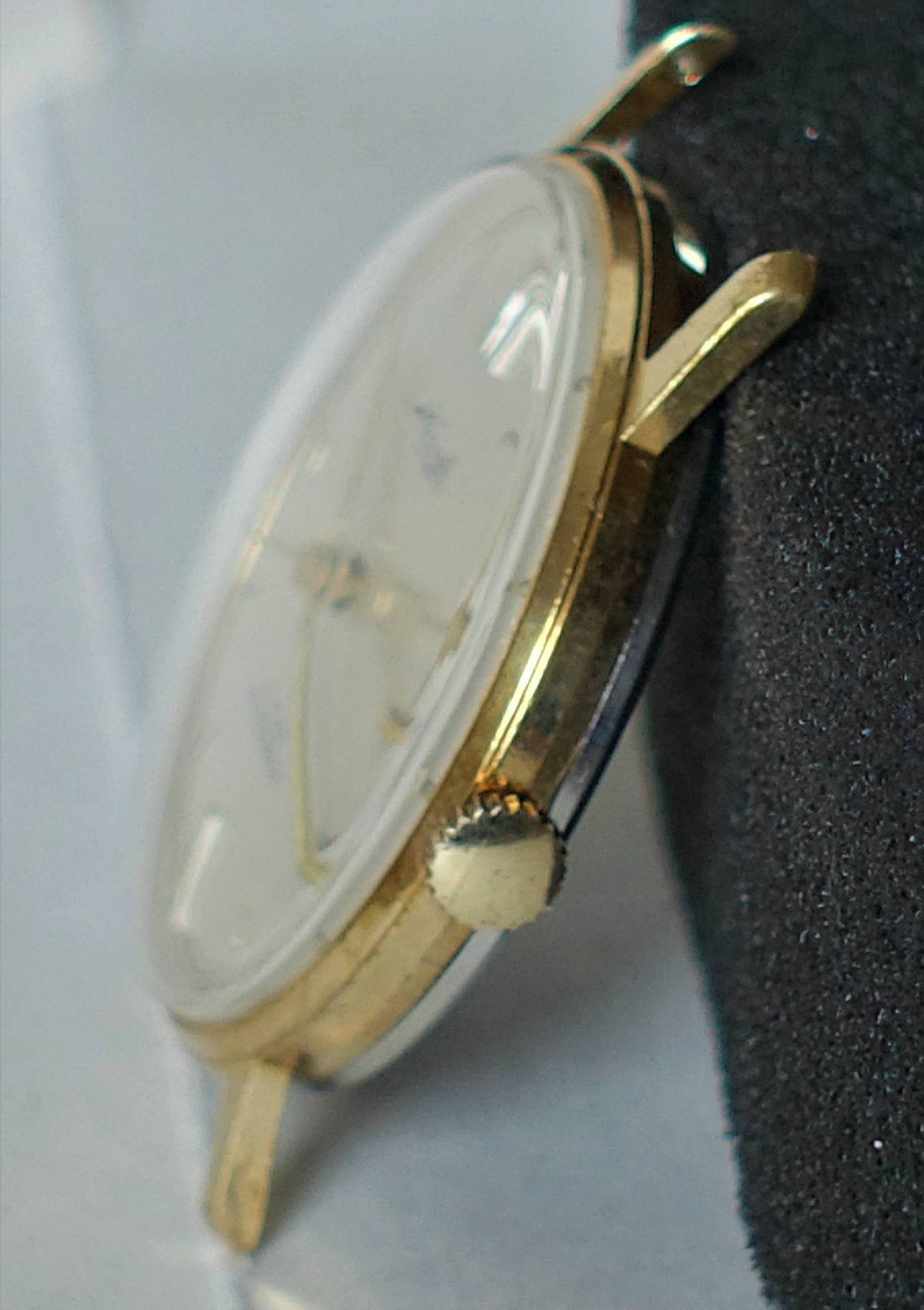 Flache Armbanduhr mit goldfarbenem Gehäuse und weißem Zifferblatt.
