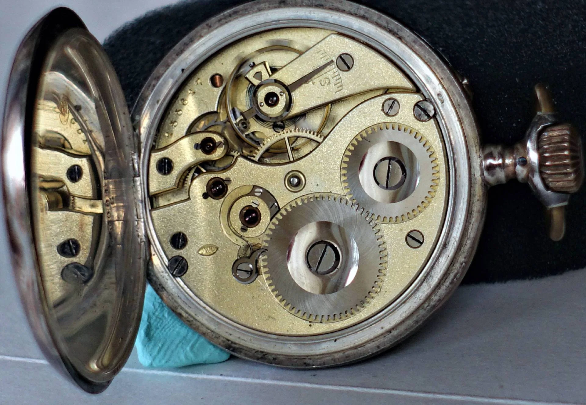 Mechanisches Uhrwerk einer Taschenuhr in silberfarbener Ausführung mit sichtbaren Zahnrädern und Aufzugskrone.