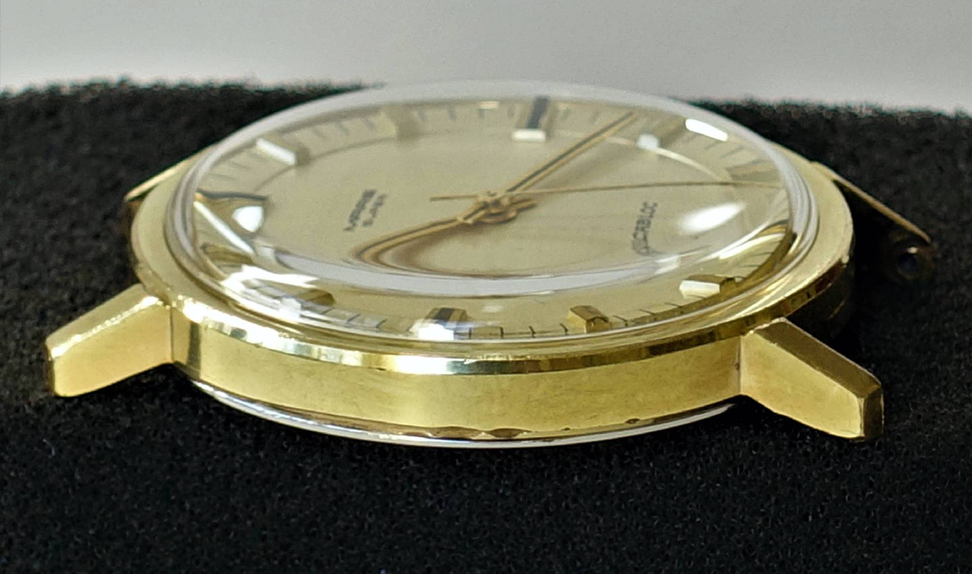 Rundes Uhrgehäuse in goldfarbener Optik mit montiertem Zifferblatt, Zeigern und Glas.