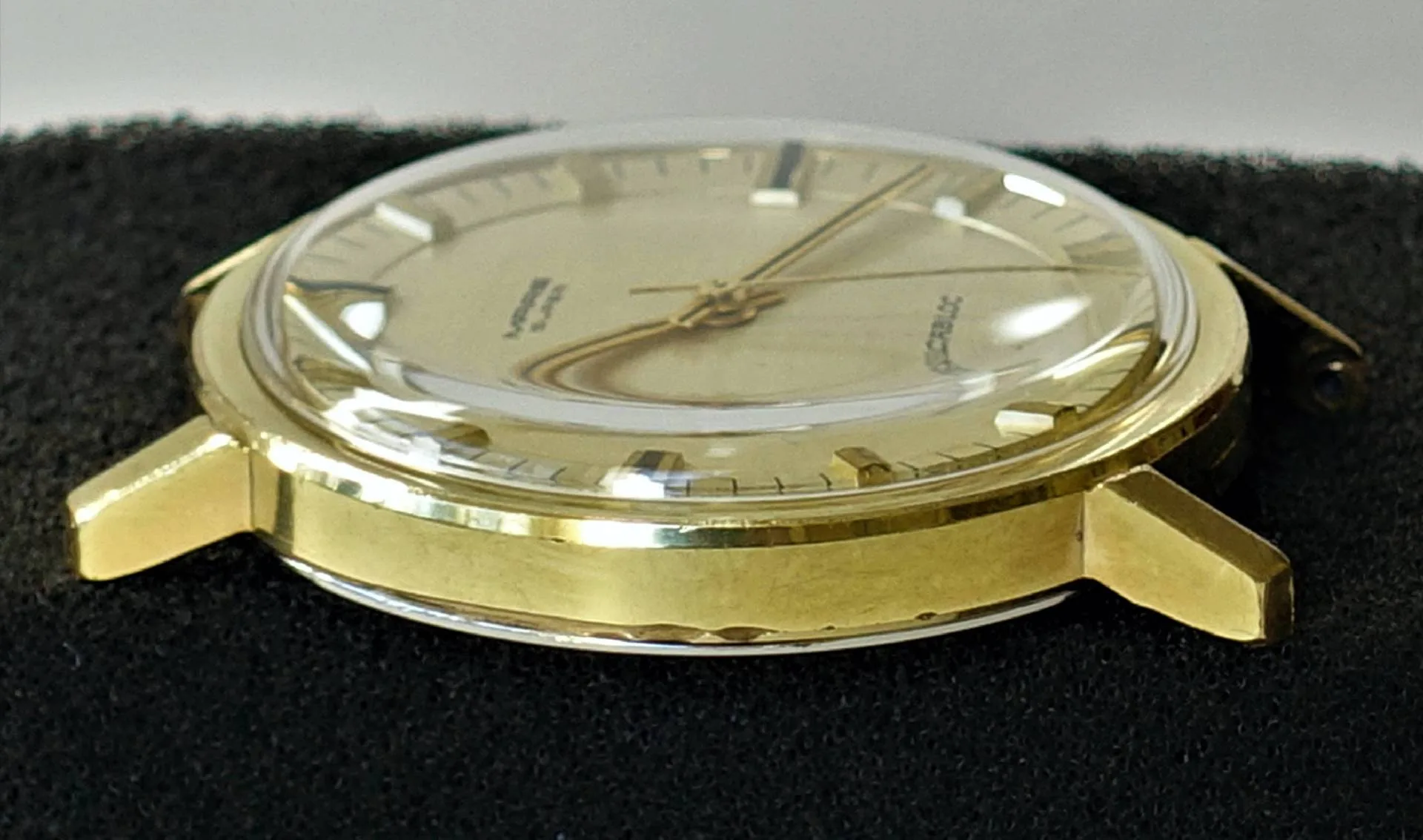 Rundes Uhrgehäuse in goldfarbener Optik mit montiertem Zifferblatt, Zeigern und Glas.
