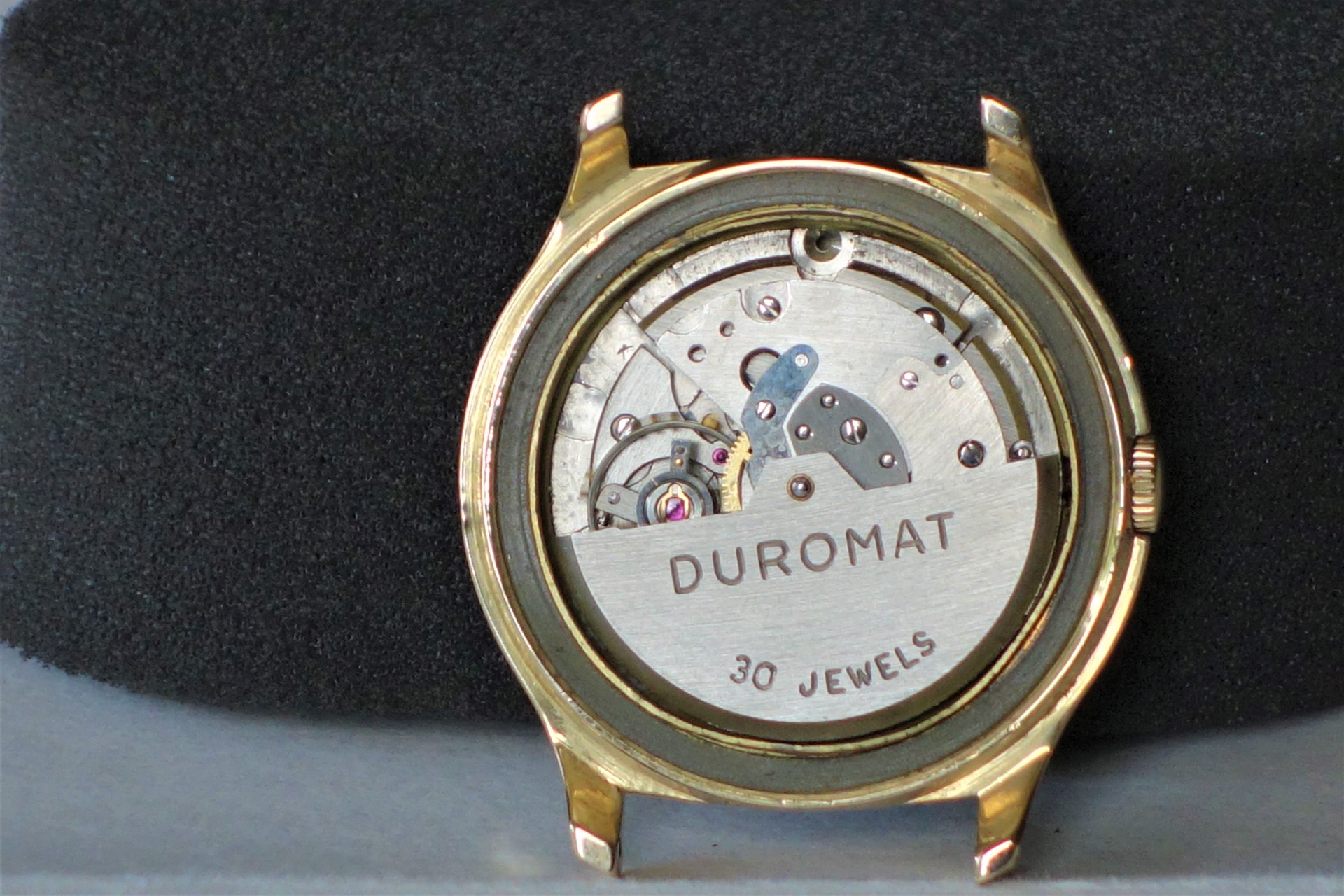 Silberfarbenes mechanisches Uhrwerk mit der Aufschrift "DUROMAT 30 JEWELS" in einem goldfarbenen Uhrengehäuse.
