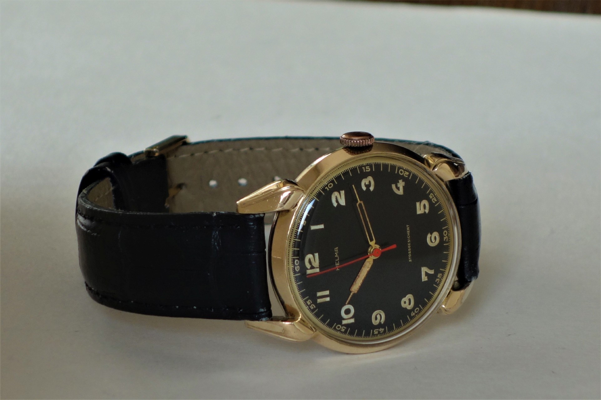 Schwarze Armbanduhr mit goldfarbenem Gehäuse und schwarzem Zifferblatt.