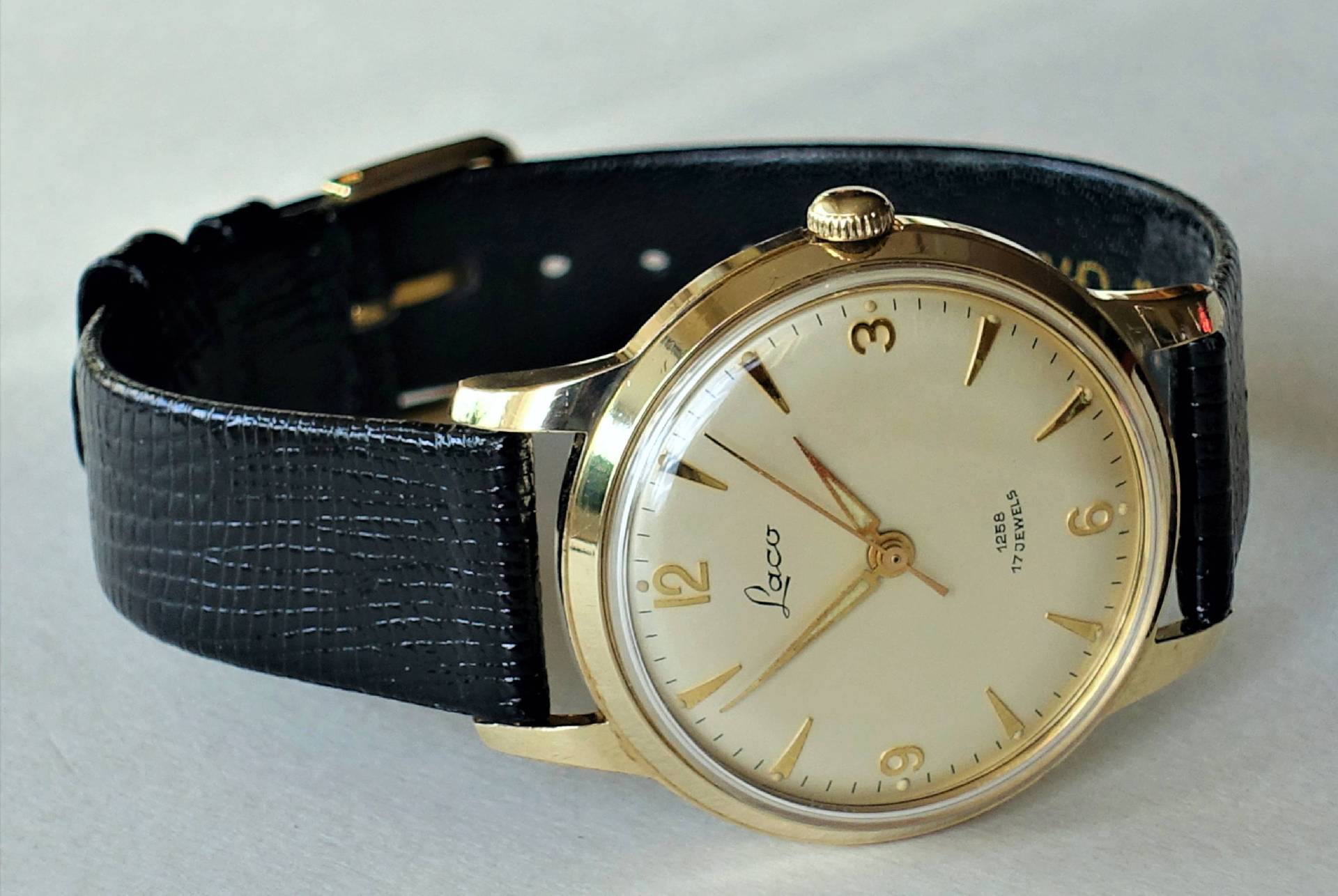 Goldfarbene Armbanduhr mit hellem Zifferblatt und schwarzem Armband.