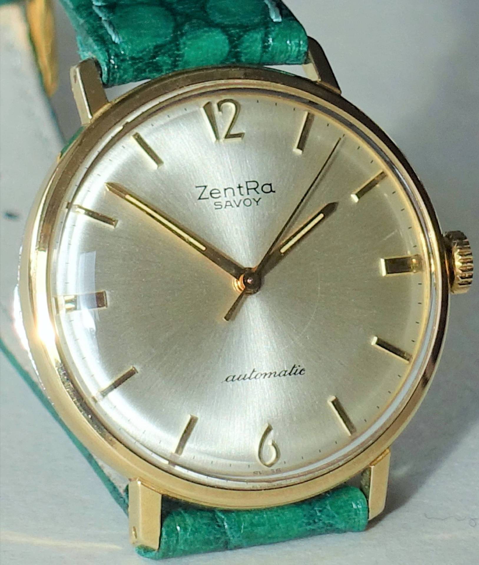 Goldfarbene Armbanduhr mit hellem Zifferblatt und grünem Armband.