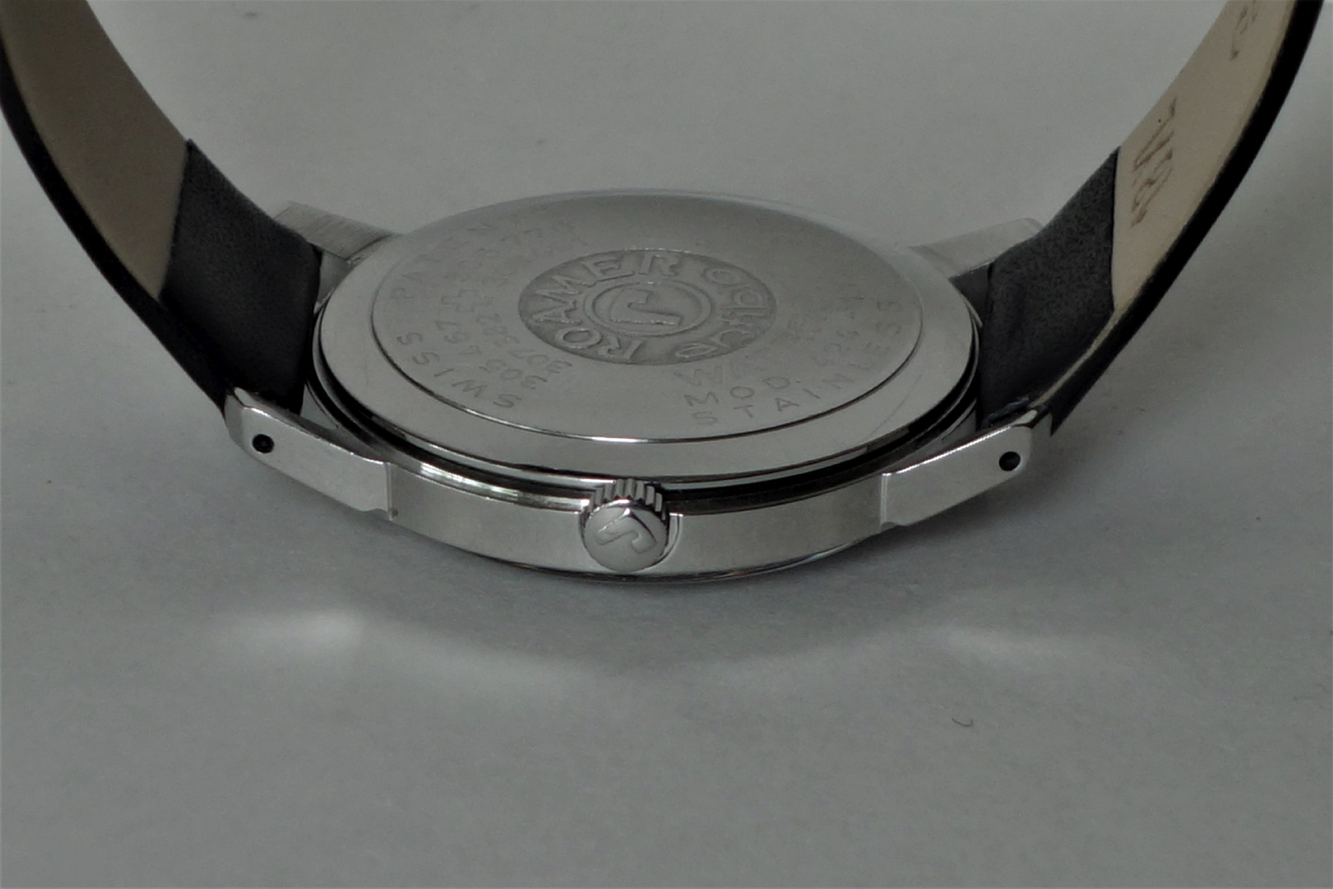 Silberfarbener Uhrenboden mit Gravur und schwarzem Lederarmband.