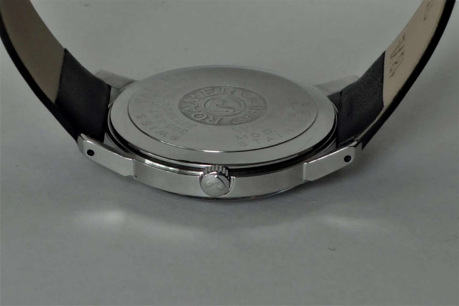 Silberfarbener Uhrenboden mit Gravur und schwarzem Lederarmband.