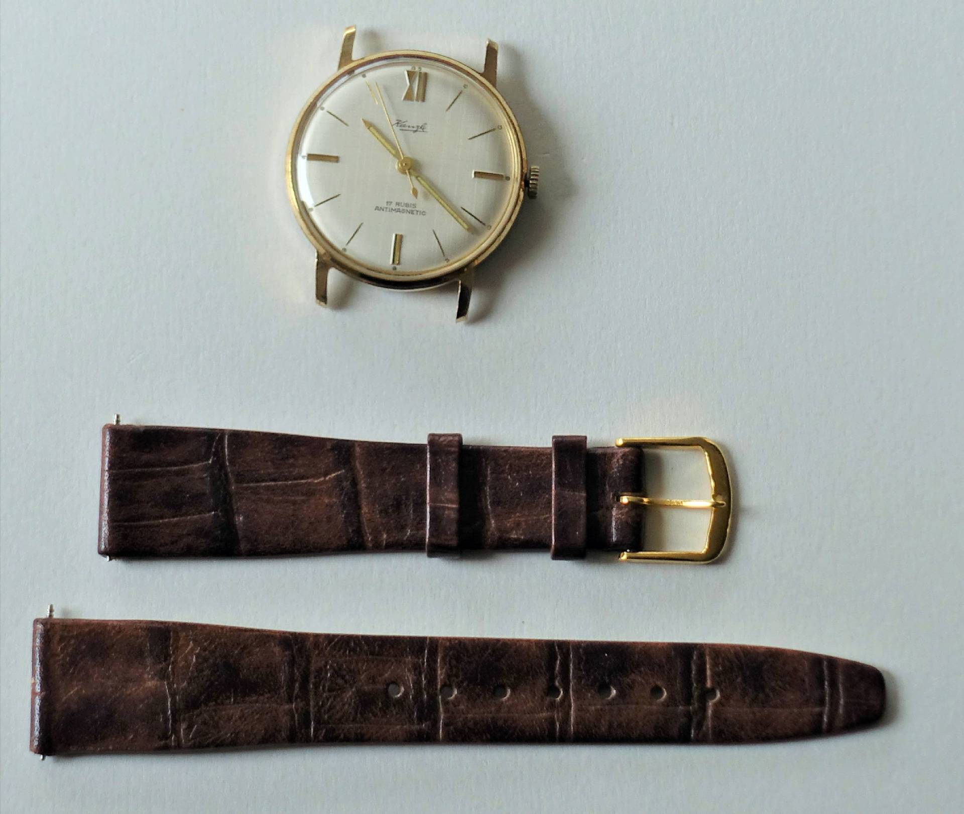 Zerlegte Armbanduhr mit goldfarbenem Gehäuse und braunem Lederarmband.