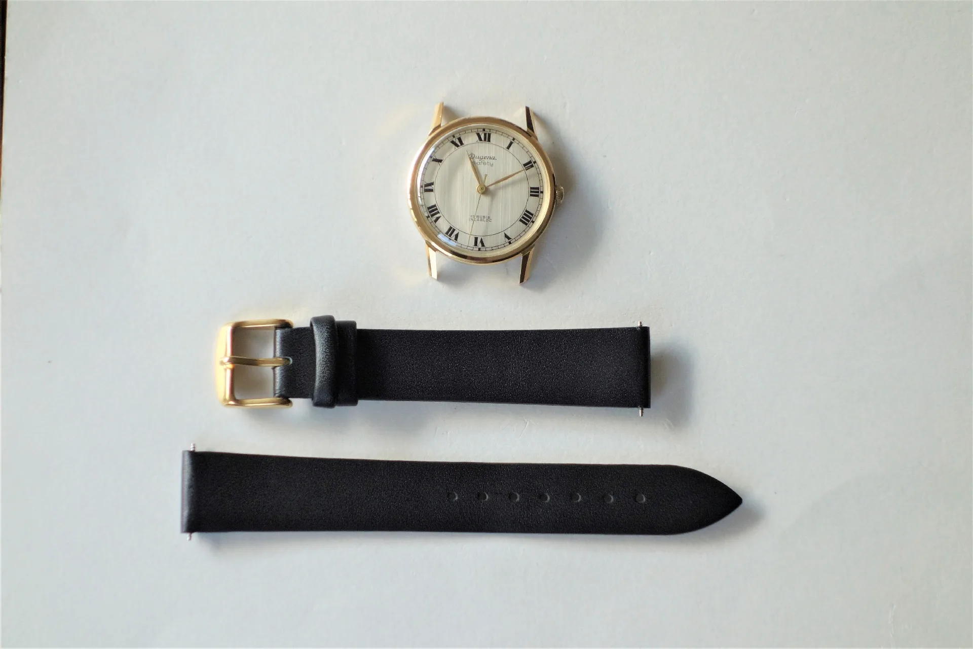 Zerlegte analoge Armbanduhr mit goldfarbenem Gehäuse und schwarzem Armband.