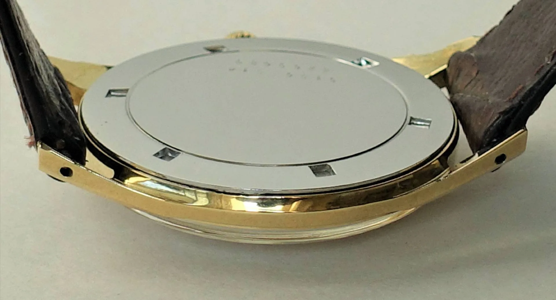 Uhrenboden silberfarben Silberfarbener Uhrenboden an einem Gehäuse mit goldfarbener Umrandung und braunem Armband.