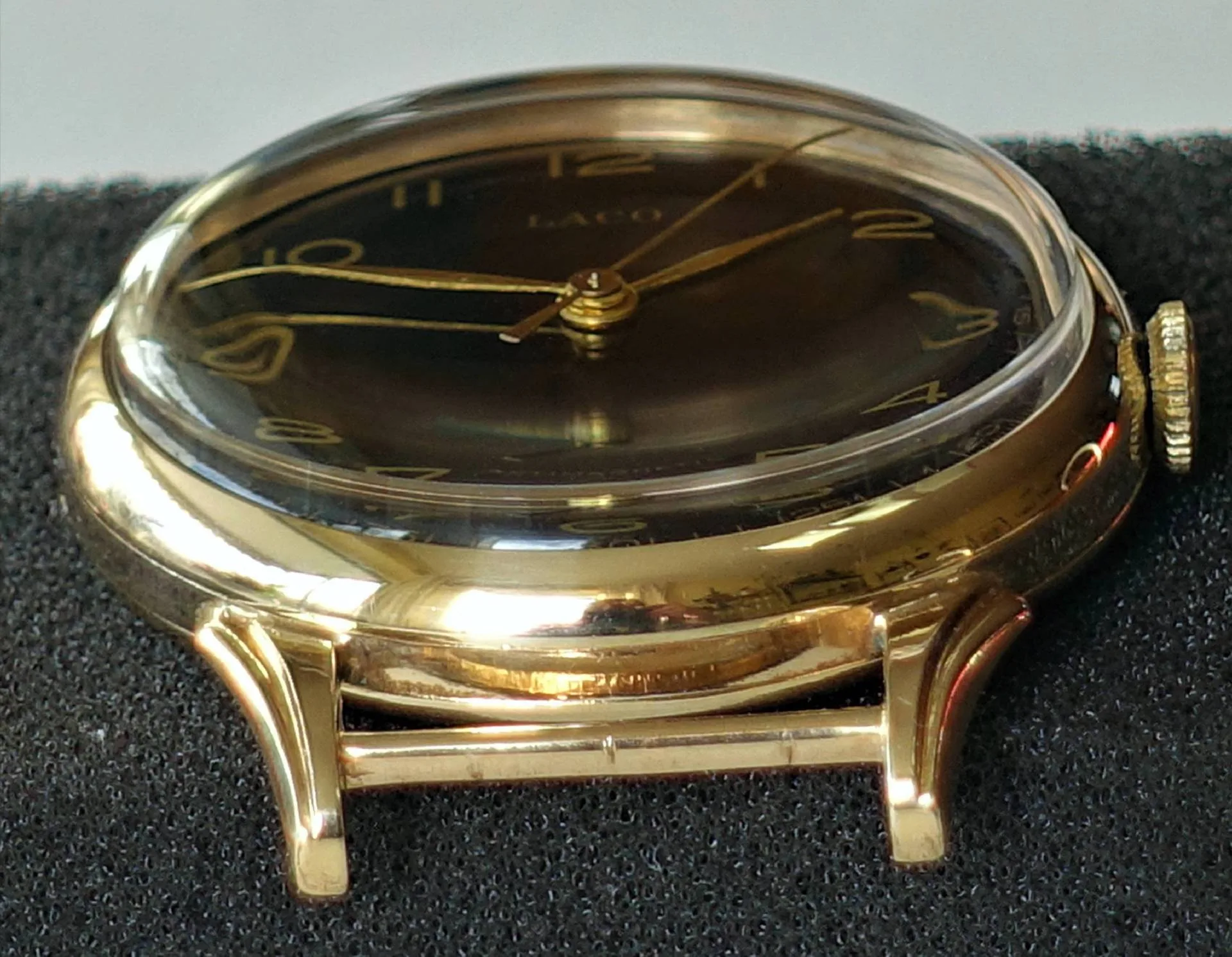 Eine flache Armbanduhr mit schwarzem Zifferblatt, gelbglänzendem Gehäuse und goldfarbenen Zeigern liegt auf schwarzem Schaumstoff.