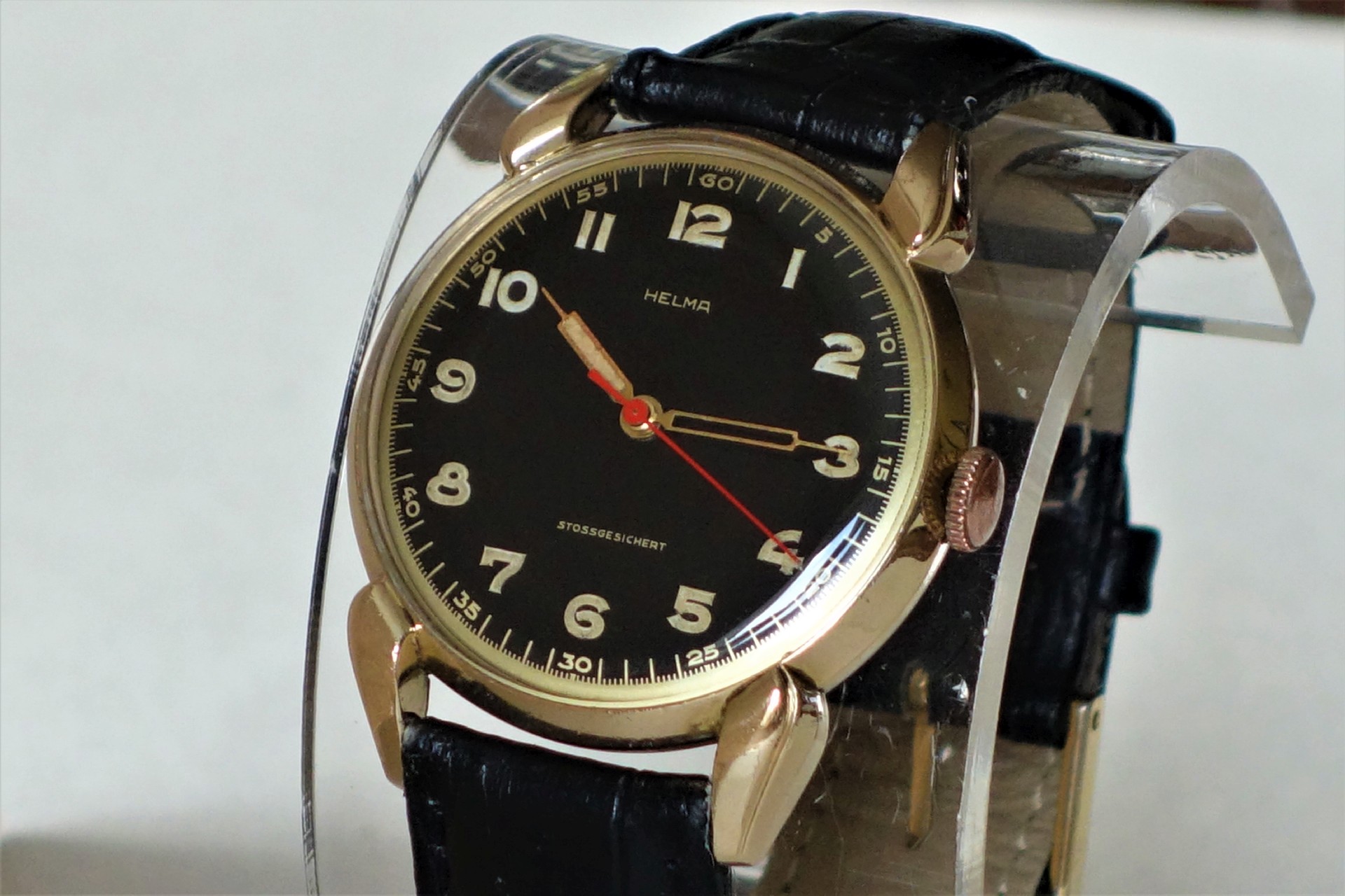 Analoge Armbanduhr mit schwarzem Zifferblatt, goldfarbenem Gehäuse und schwarzem Armband.