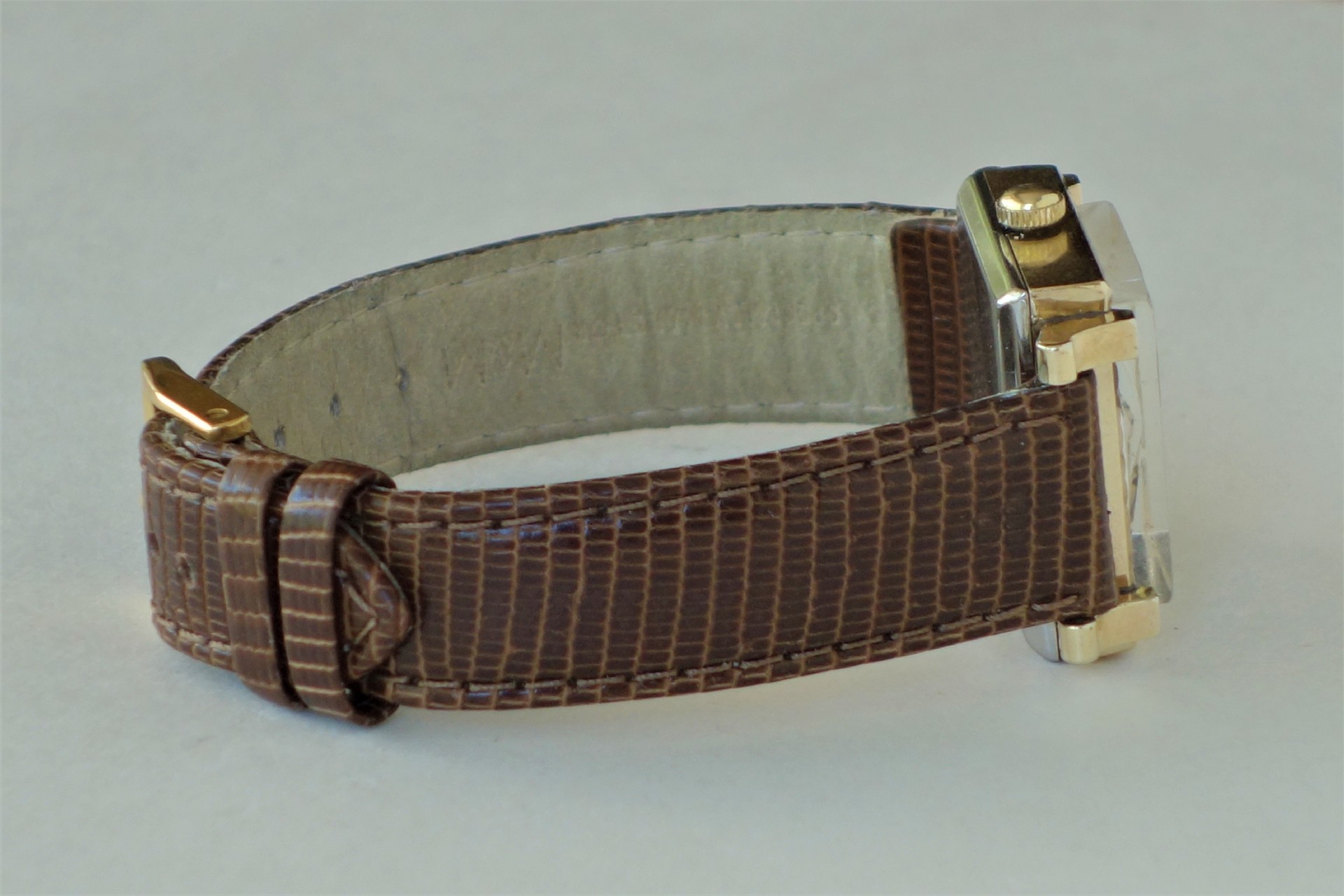 Rechteckige Armbanduhr mit braunem Lederarmband und goldfarbenen Elementen.