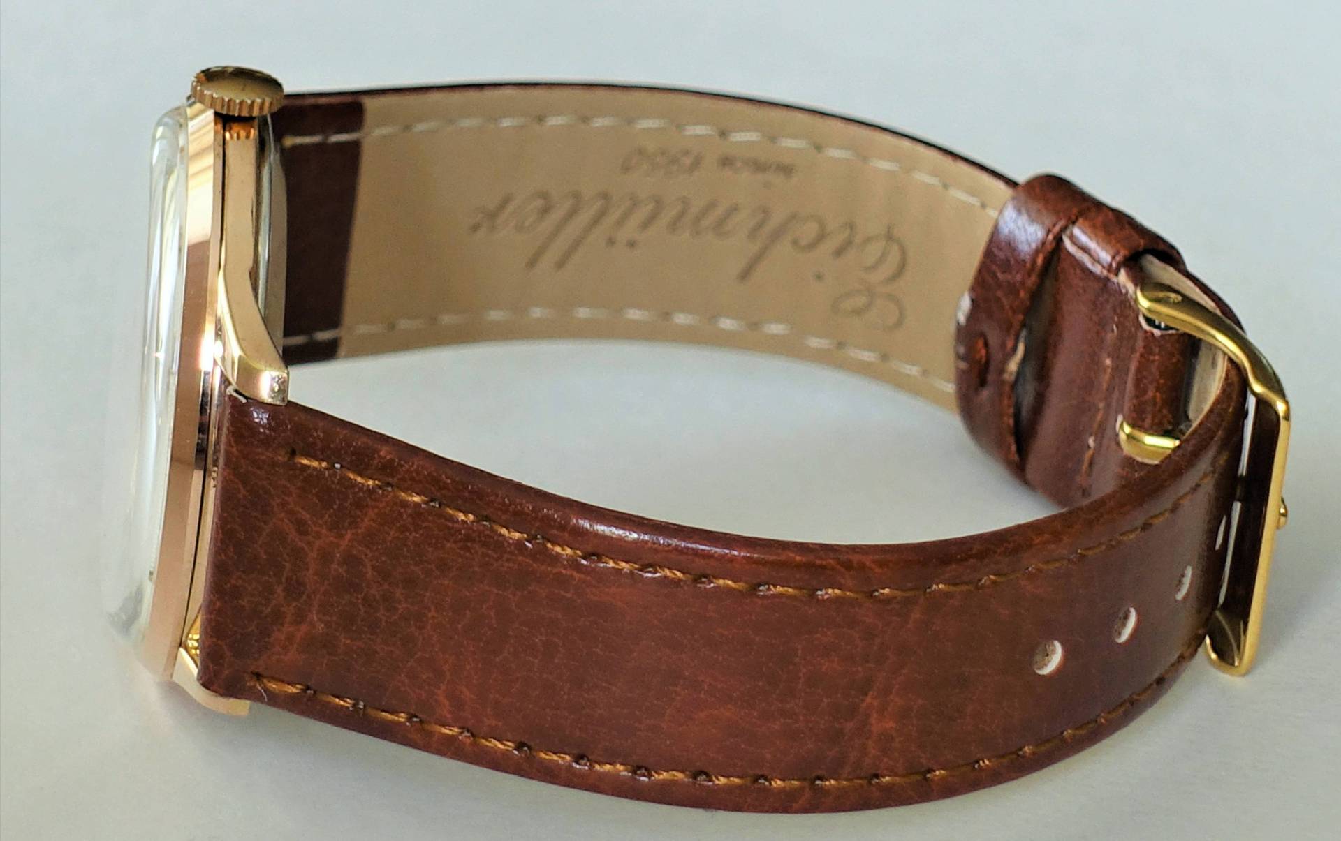 Eine Armbanduhr mit braunem Lederarmband, roségoldfarbenem Gehäuse und goldfarbener Dornschließe liegt auf einer hellen Oberfläche.