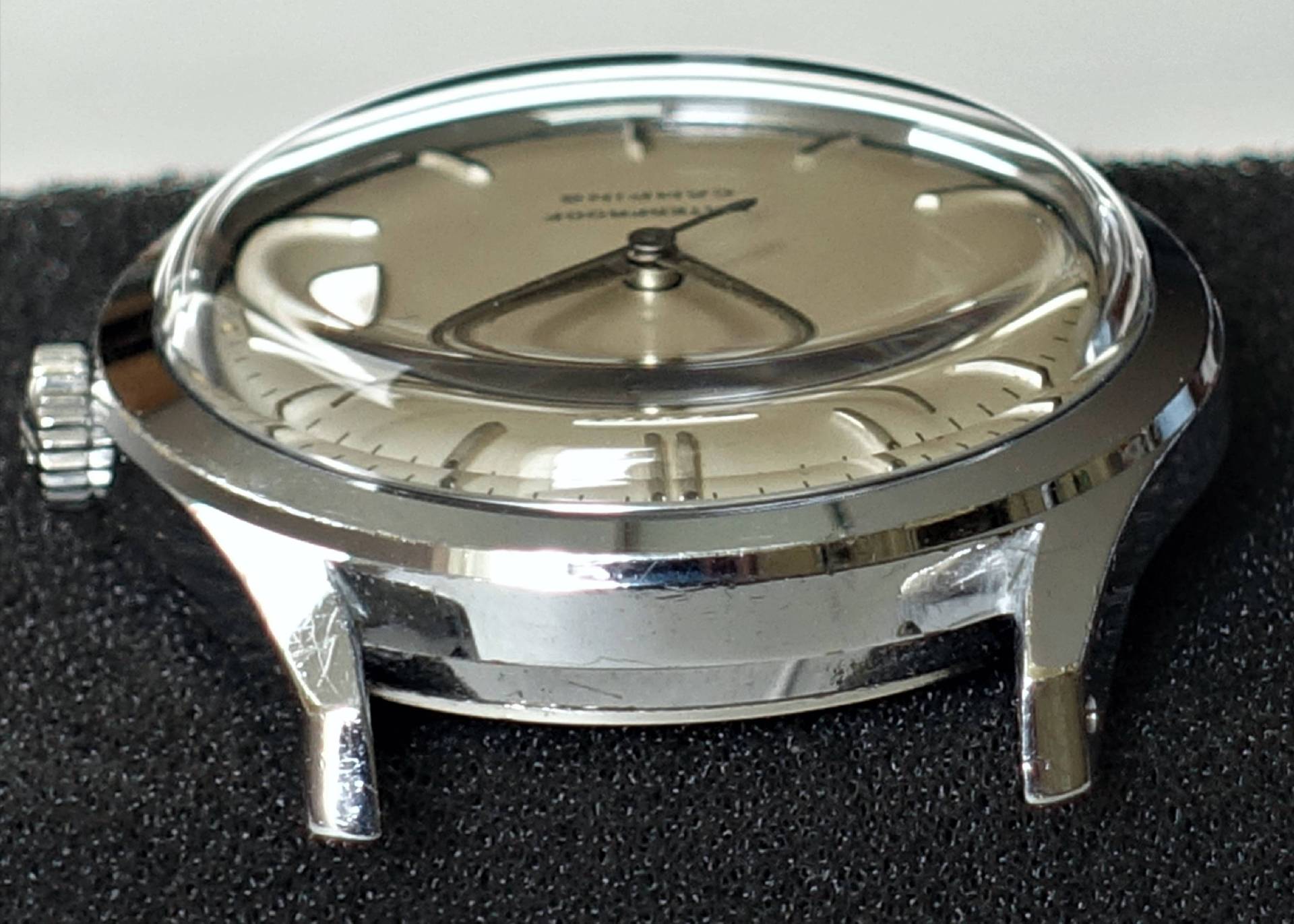 Silberfarbenes Gehäuse einer Armbanduhr mit hellem Zifferblatt und aufgesetztem Glas.