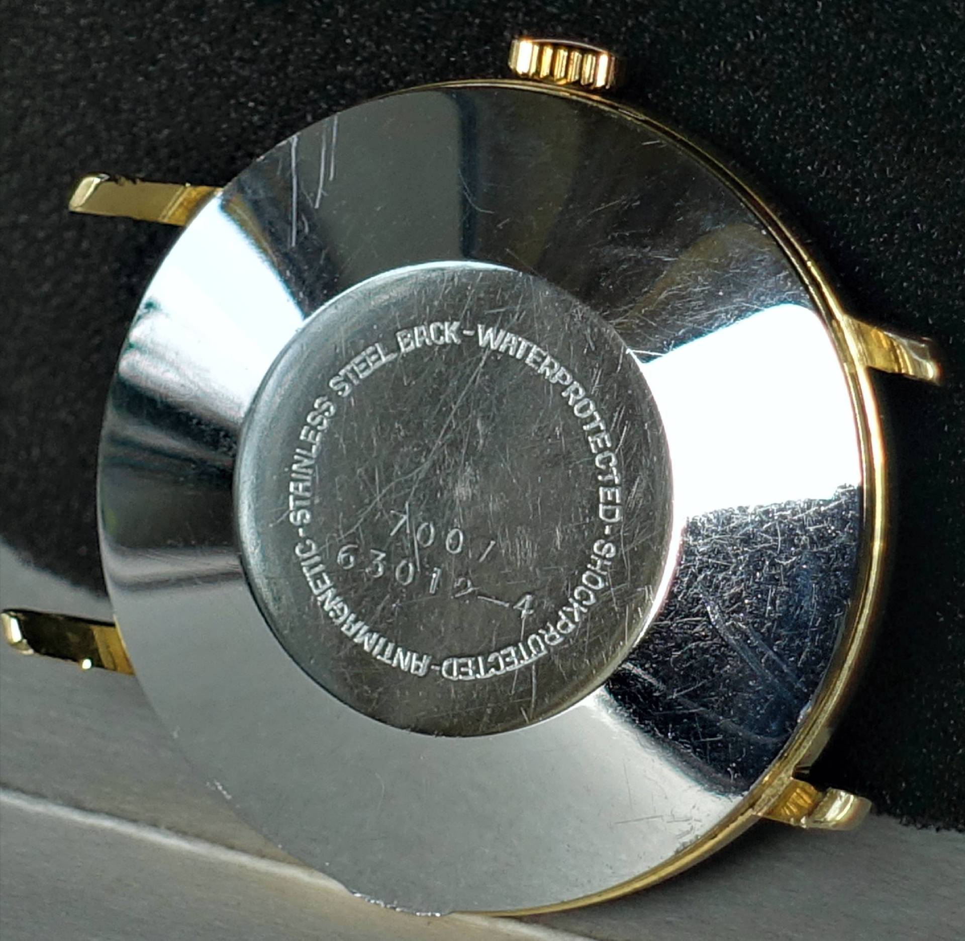 Silberfarbene Rückseite eines Uhrgehäuses mit goldfarbenen Hörnern und Krone.