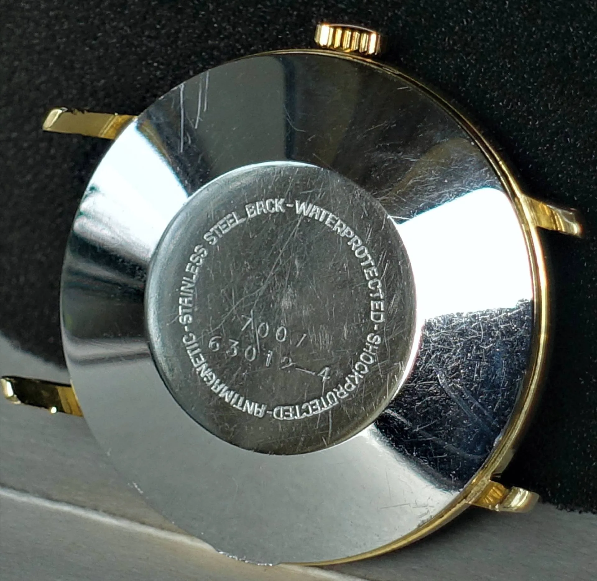 Silberfarbene Rückseite eines Uhrgehäuses mit goldfarbenen Hörnern und Krone.