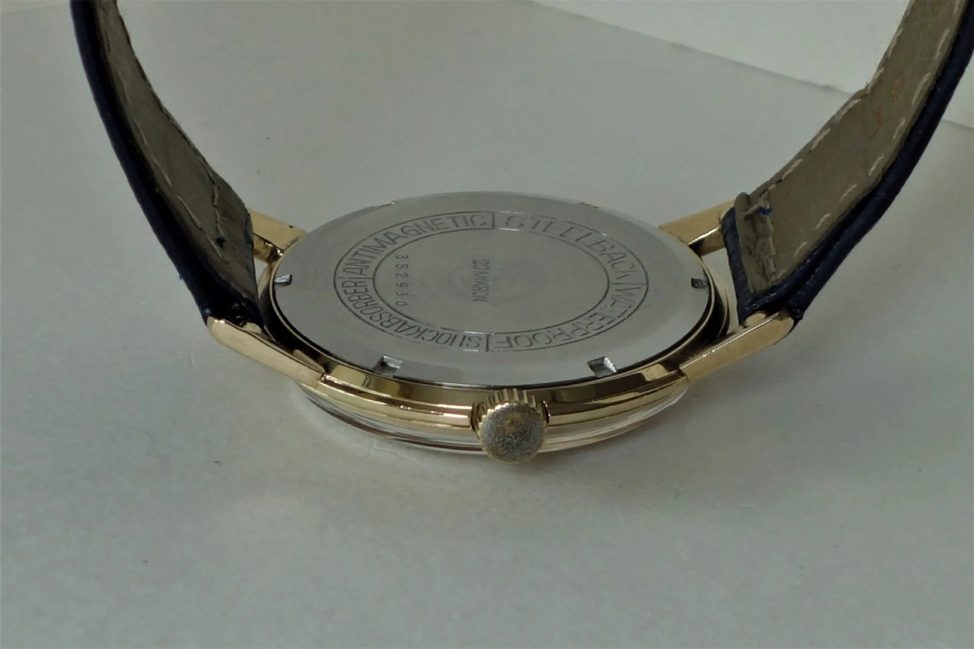 Silberfarbener Uhrboden mit Gravur und seitlicher goldfarbener Krone, befestigt an einem dunklen Armband.
