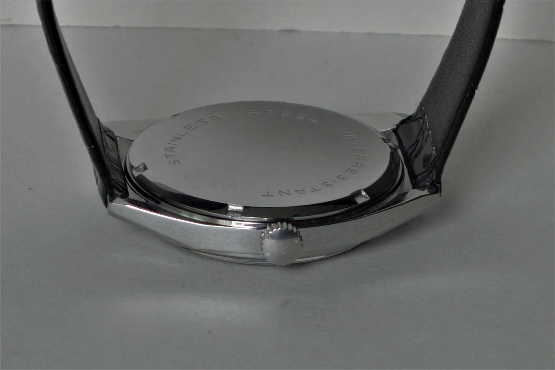 Silberfarbener runder Uhrenboden mit seitlicher Krone und schwarzem Armband.