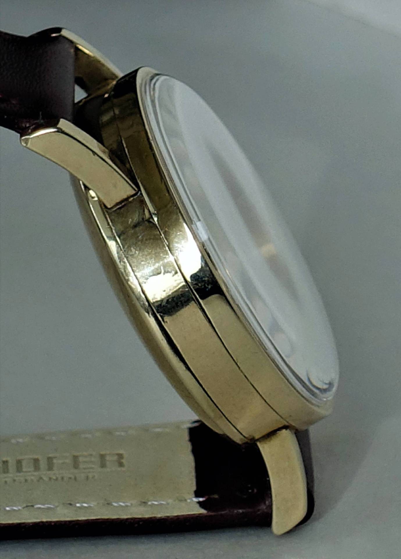 Detailansicht einer eleganten Herrenuhr mit goldnem Gehäuse und braunem Lederarmband