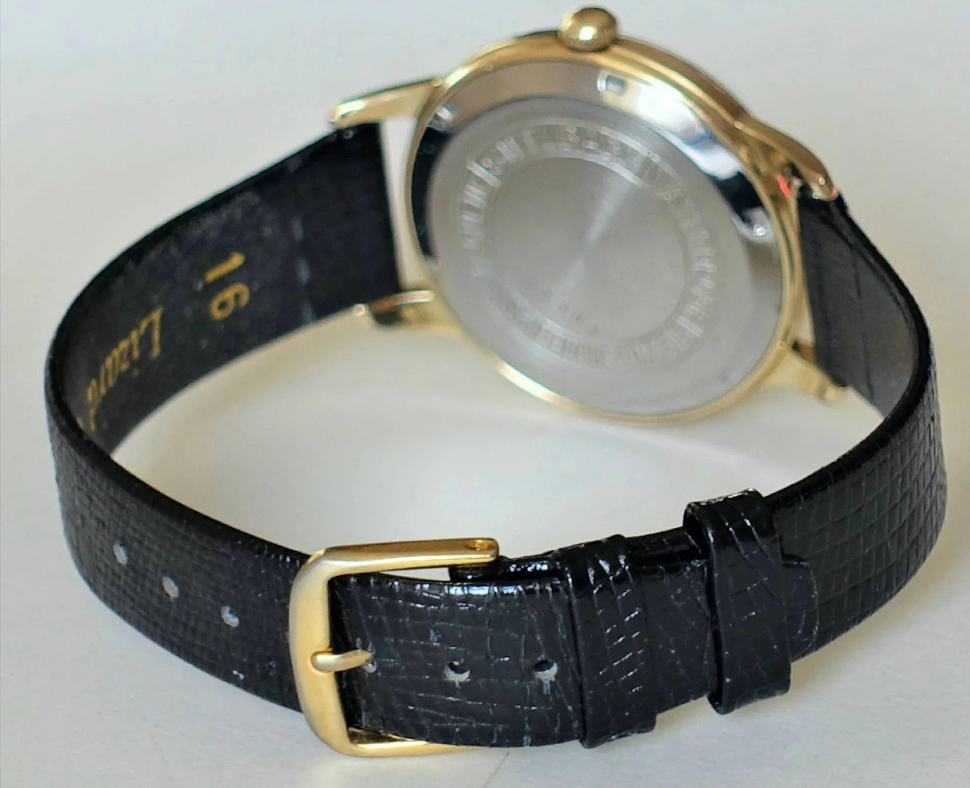 Armbanduhr schwarz goldfarben Armbanduhr mit schwarzem Armband und goldfarbenem Gehäuse, Rückseite sichtbar.