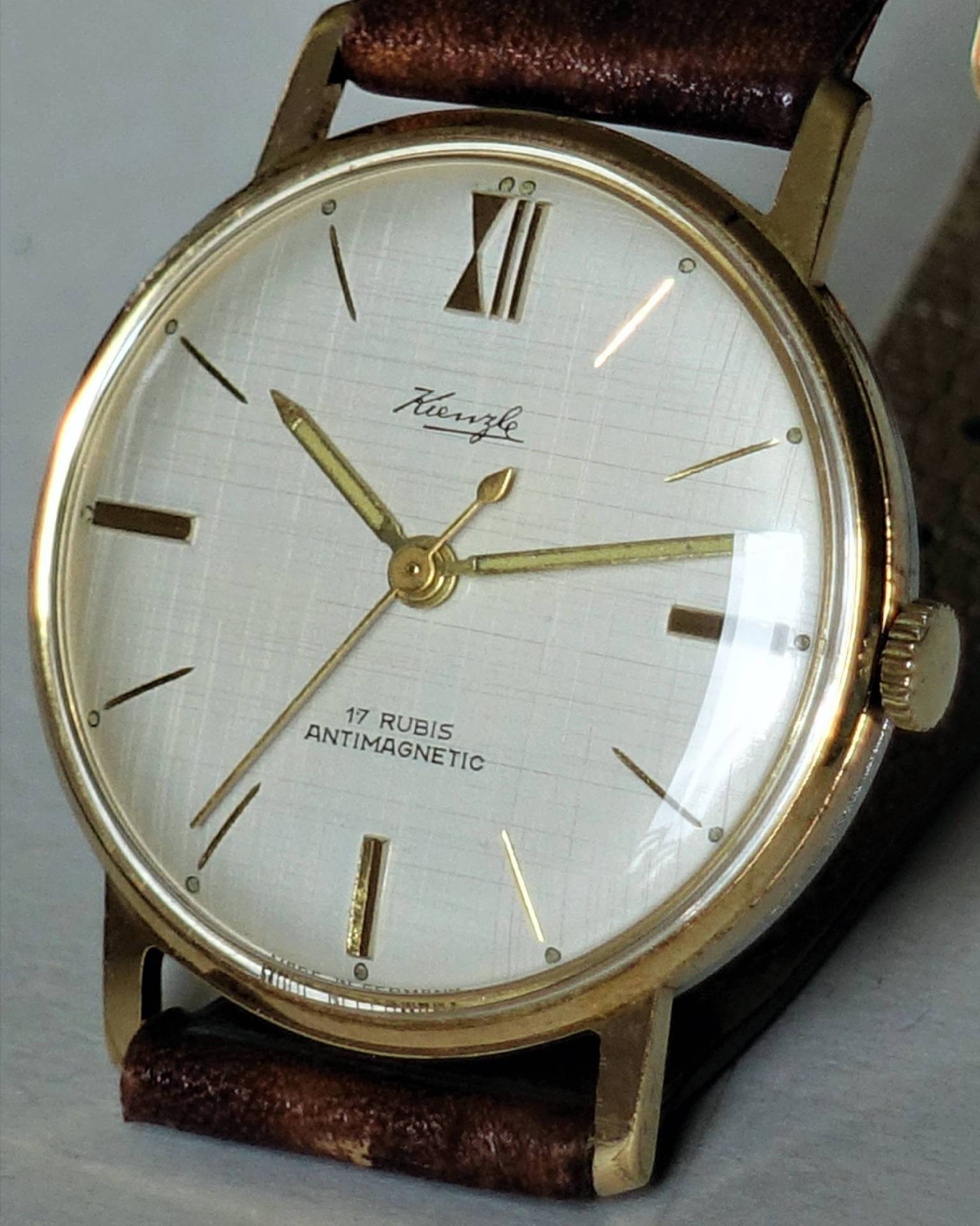 Goldfarbene Armbanduhr mit weißem Zifferblatt, braunem Armband und der Aufschrift "Kienzle 17 Rubis Antimagnetic".
