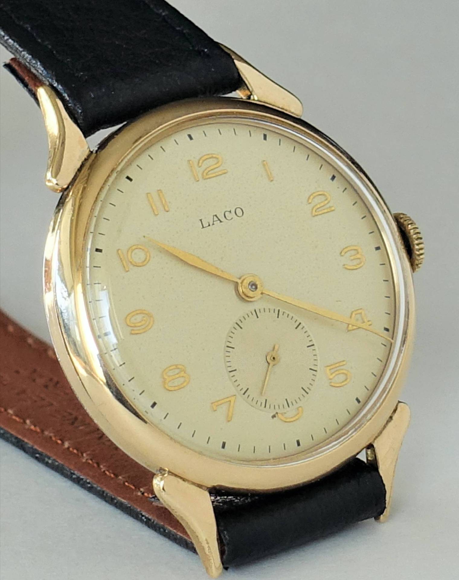 Goldfarbene Armbanduhr mit hellem Zifferblatt und schwarzem Armband.