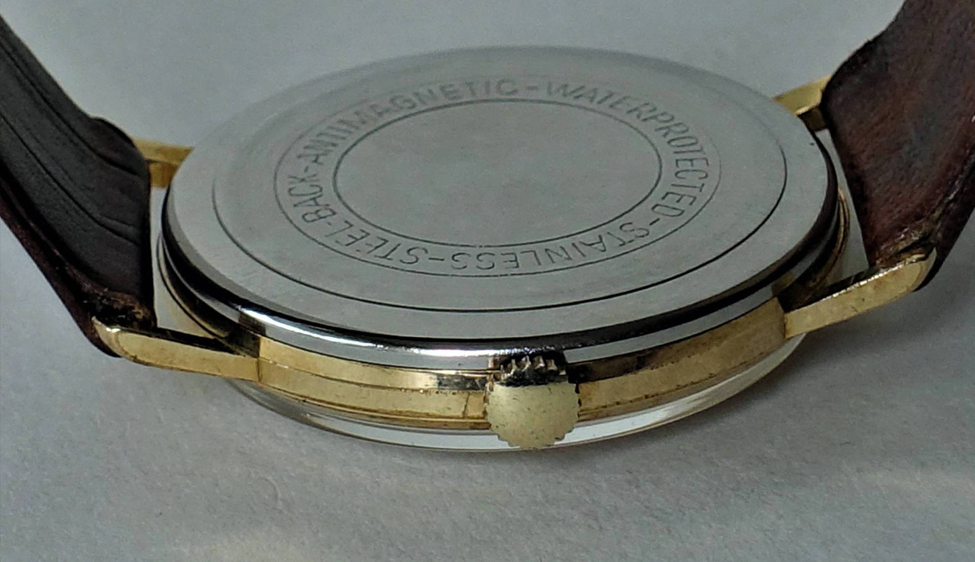 Silberfarbener Uhrenboden mit Gravur an einer Armbanduhr mit braunem Armband.