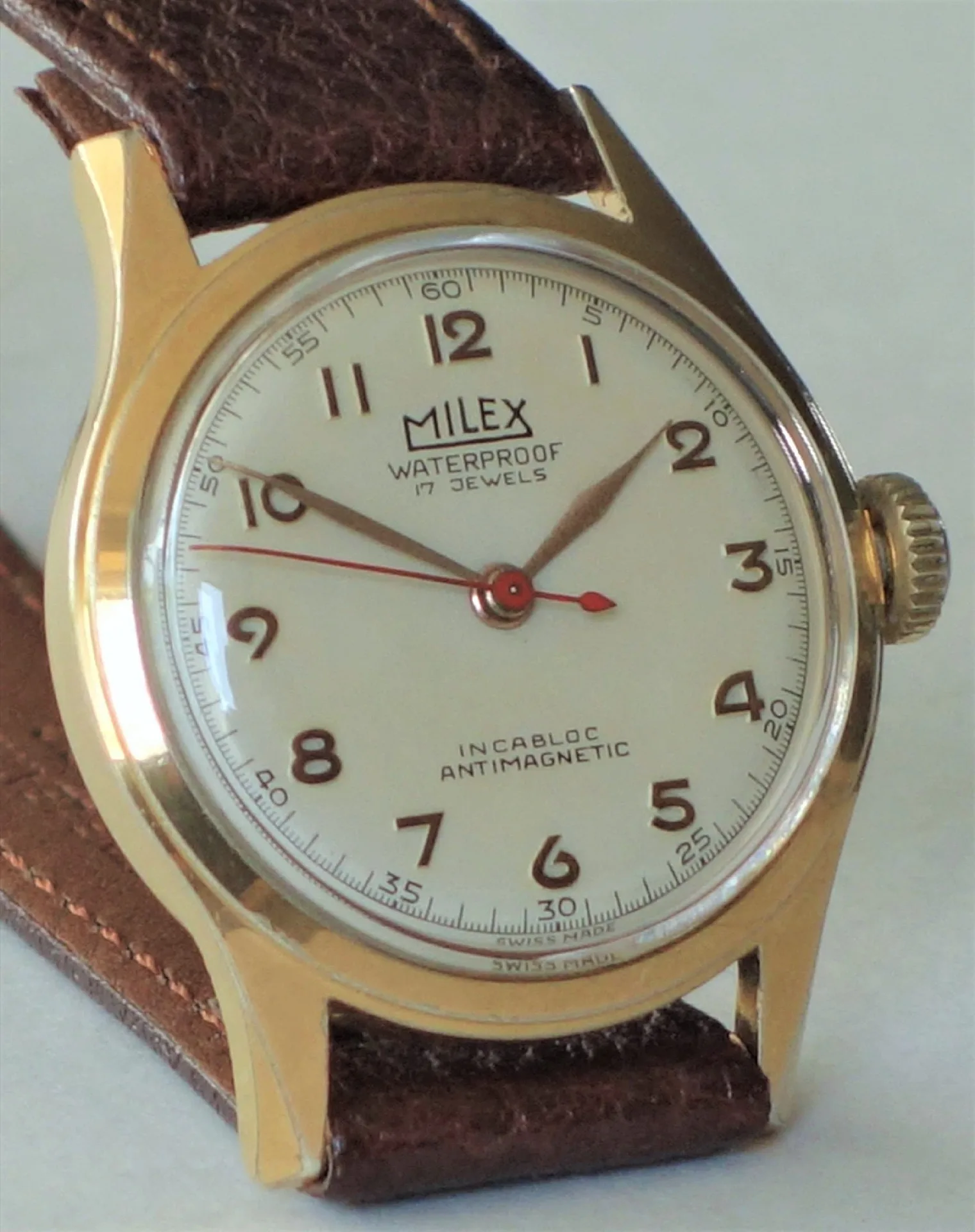 Analoge Armbanduhr der Marke Milex mit goldfarbenem Gehäuse und braunem Armband.