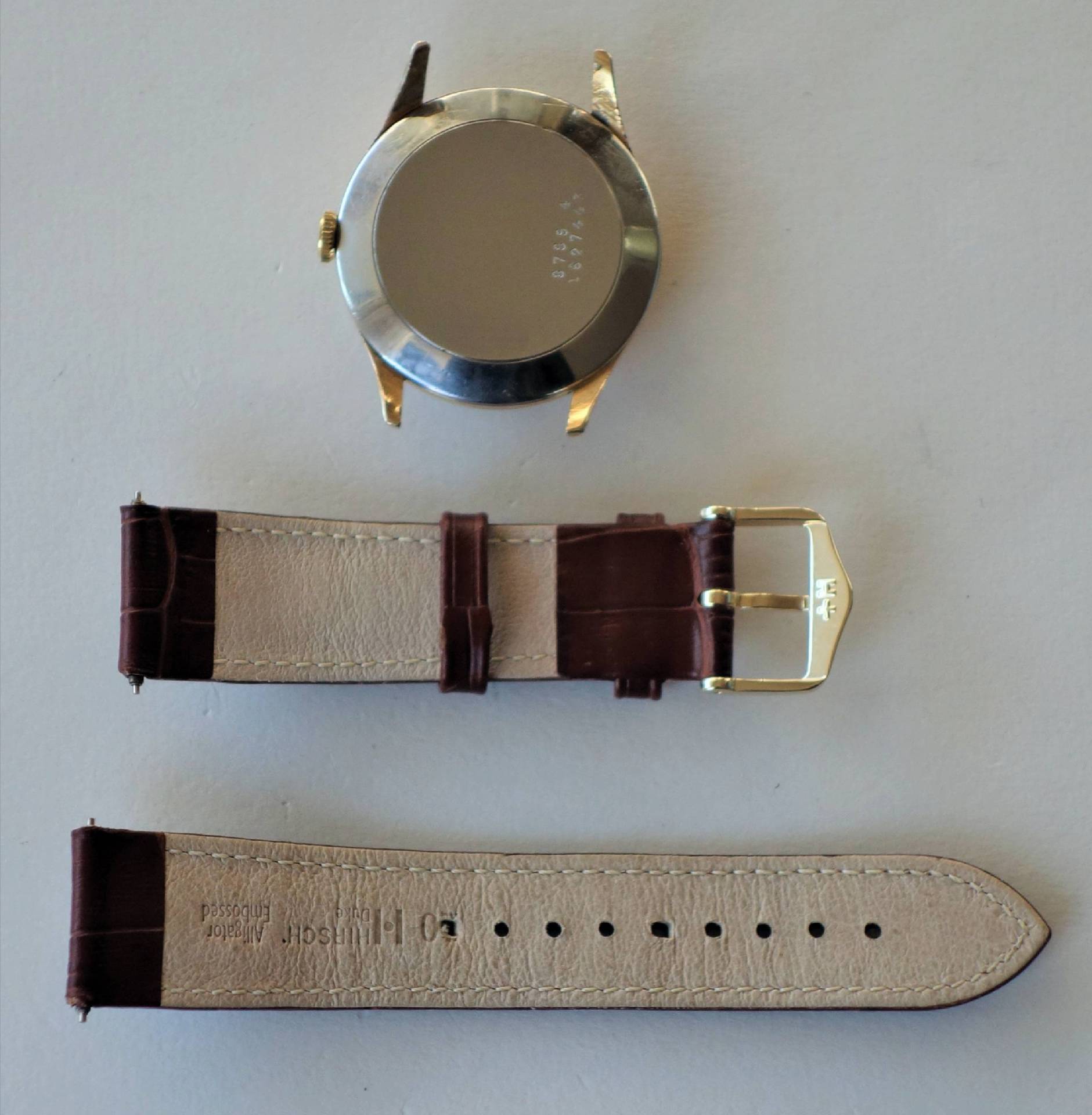 Rundes Uhrgehäuse in silber und gold mit braunem Lederarmband und goldfarbener Dornschließe.