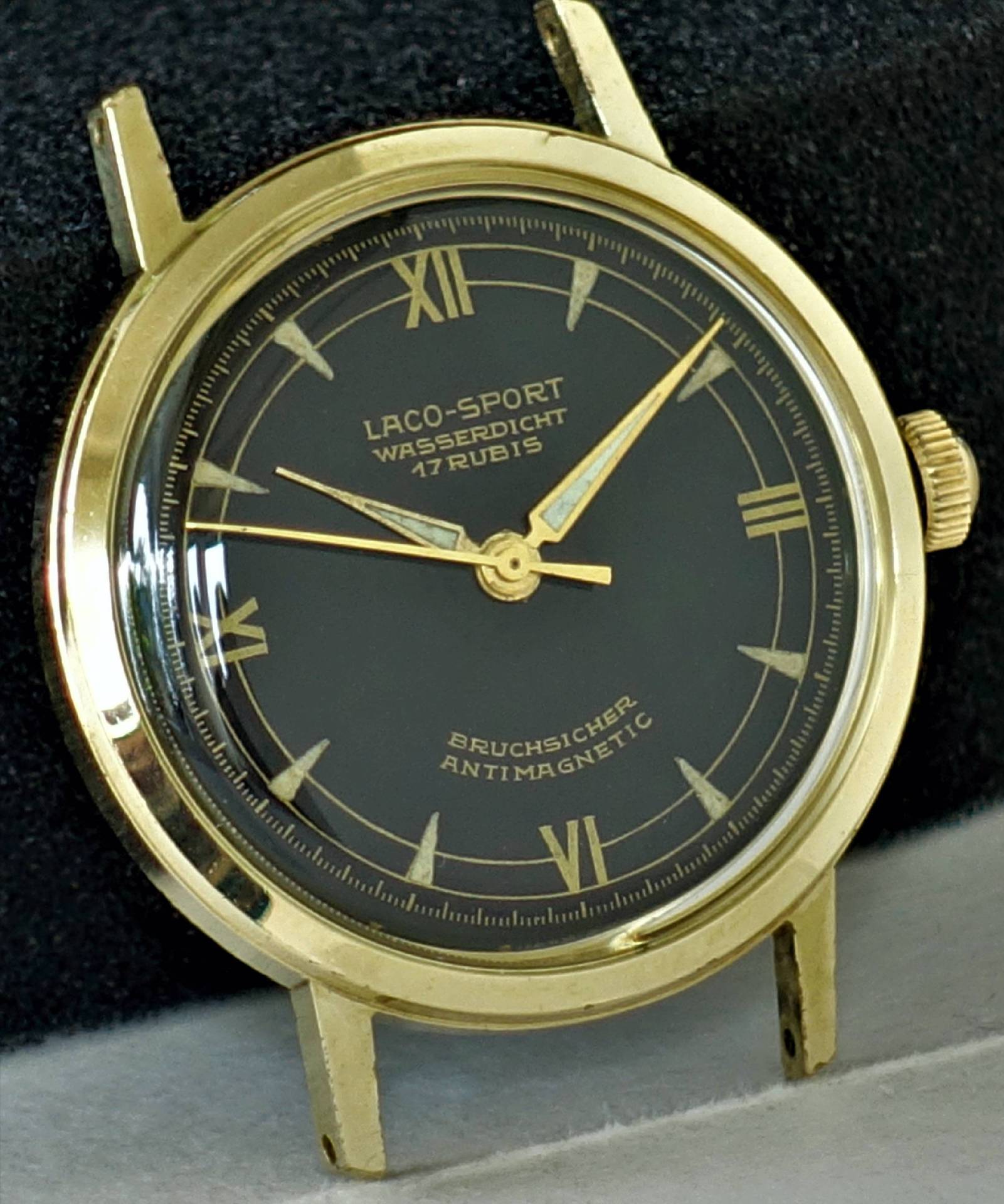 Schwarze Armbanduhr mit goldfarbenem Gehäuse und goldfarbenen Zeigern, römische Ziffern auf dem Zifferblatt.