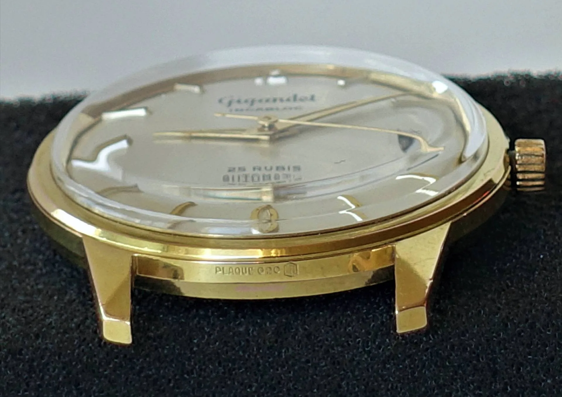 Eine Armbanduhr mit glänzend gelbfarbenem Gehäuse, hellem Zifferblatt und goldfarbenen Zeigern liegt auf schwarzem Stoff.