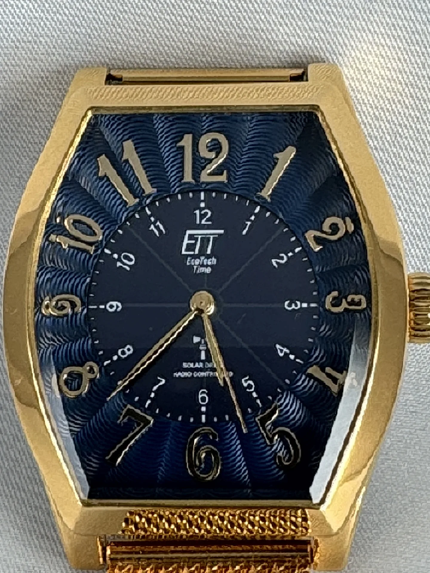 Goldene Tonneau Solar-Armbanduhr Goldfarbene Armbanduhr mit tonneauförmigem Gehäuse und blauem Zifferblatt mit goldenen Zahlen.