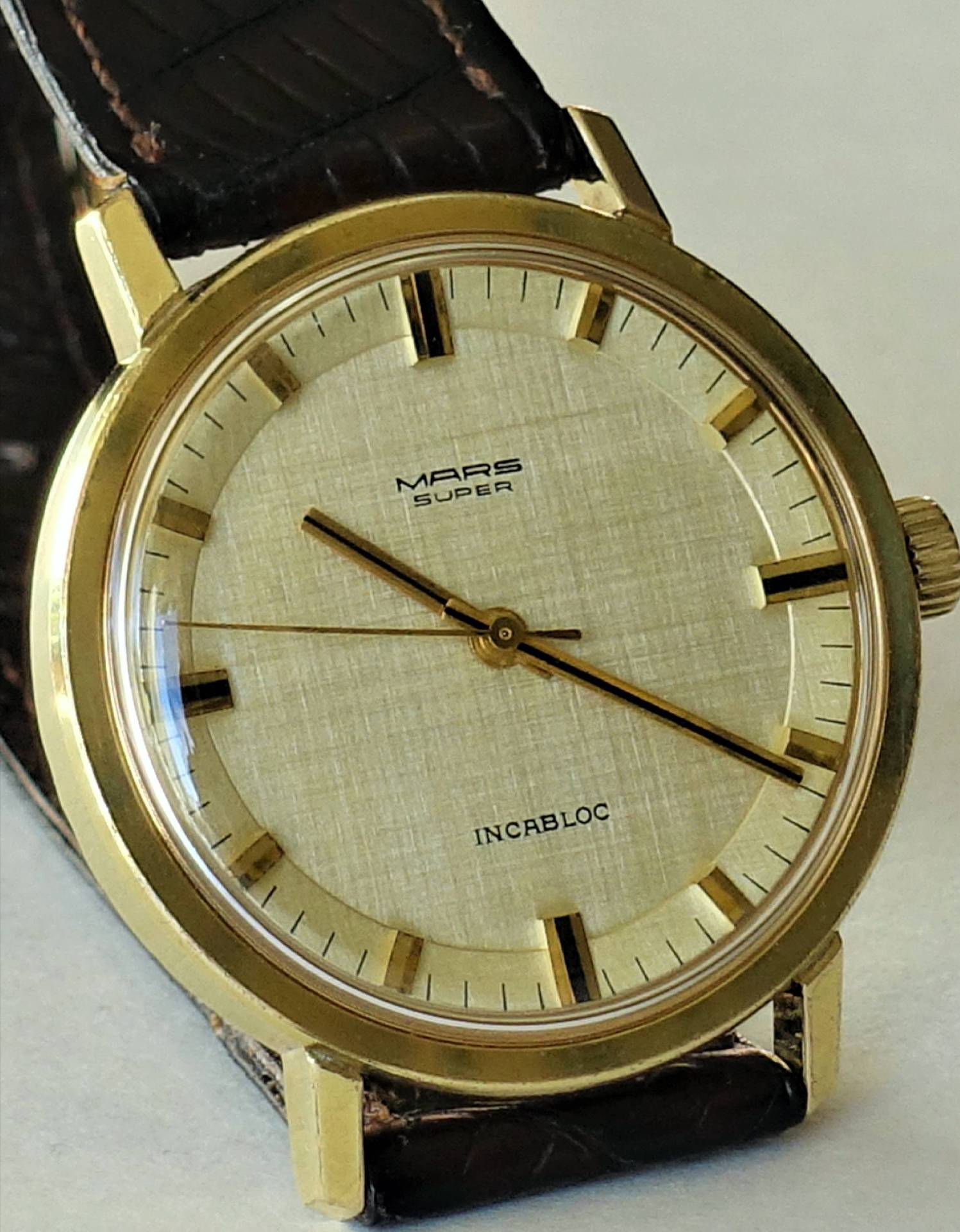 Goldfarbene Mars Super Armbanduhr mit hellem Zifferblatt und braunem Armband.