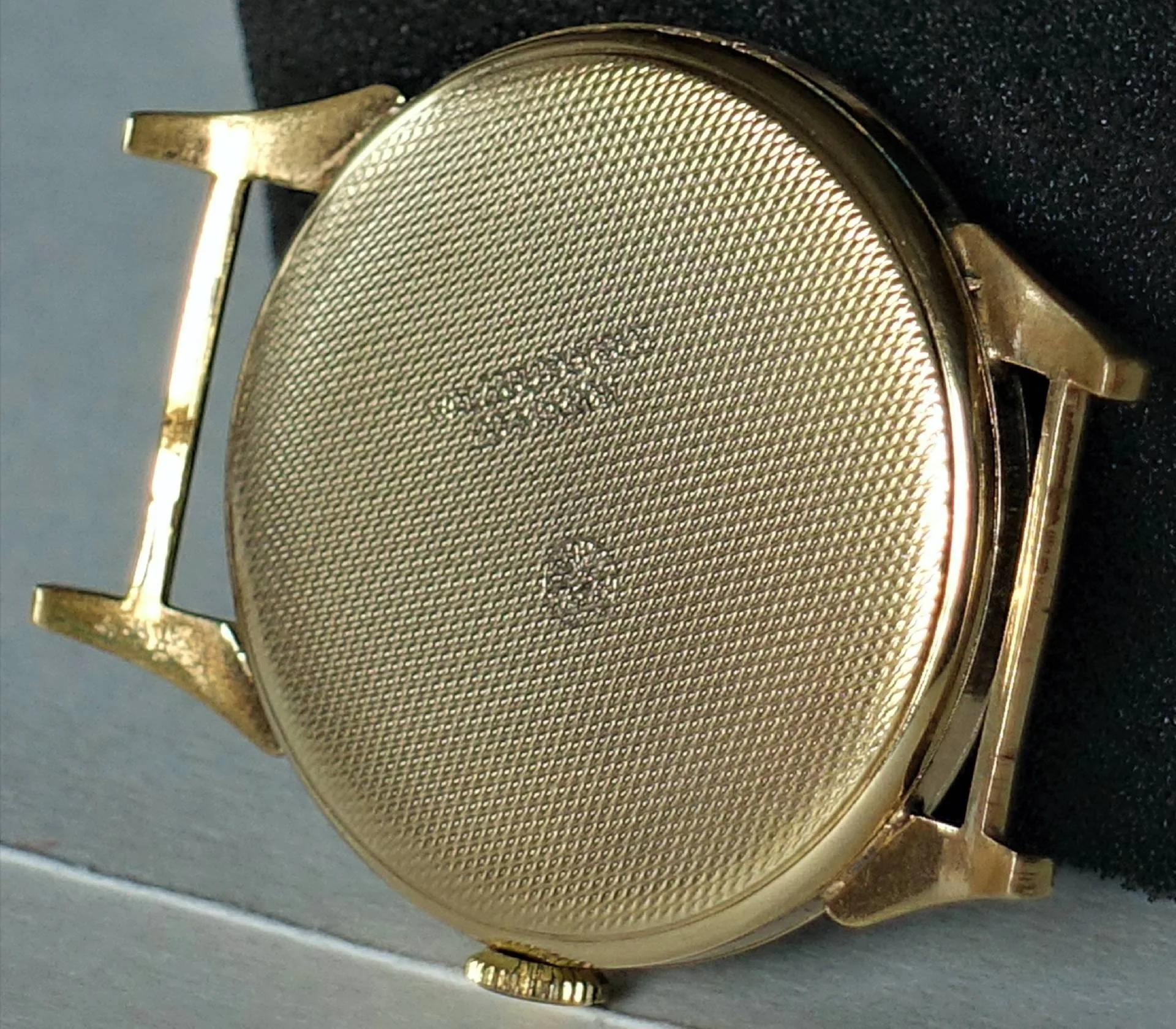 Die Rückseite eines fein gravierten, gelb-metallisch glänzenden Uhrengehäuses ohne Armband ist zu sehen.