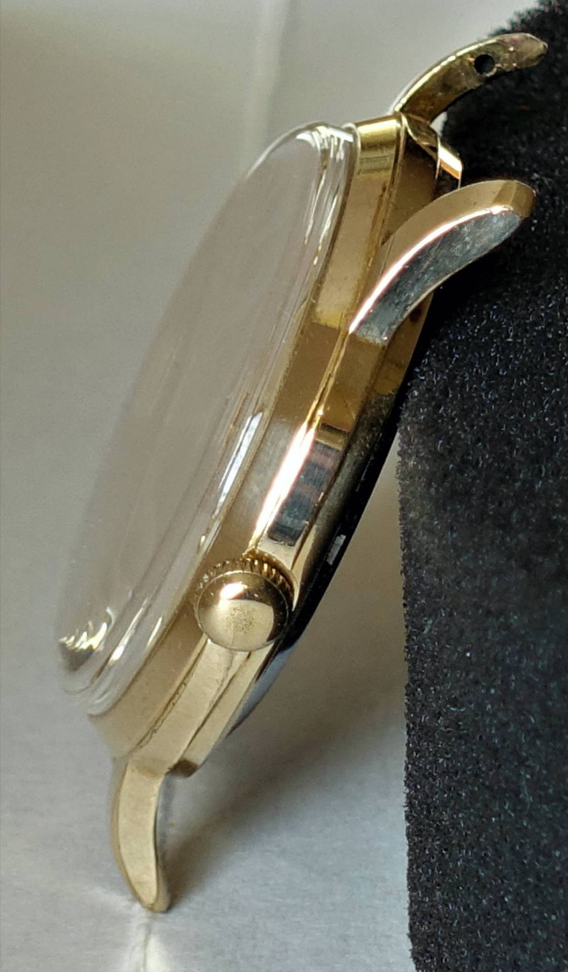 Goldfarbenes Uhrgehäuse mit transparenter Abdeckung und seitlicher Krone.