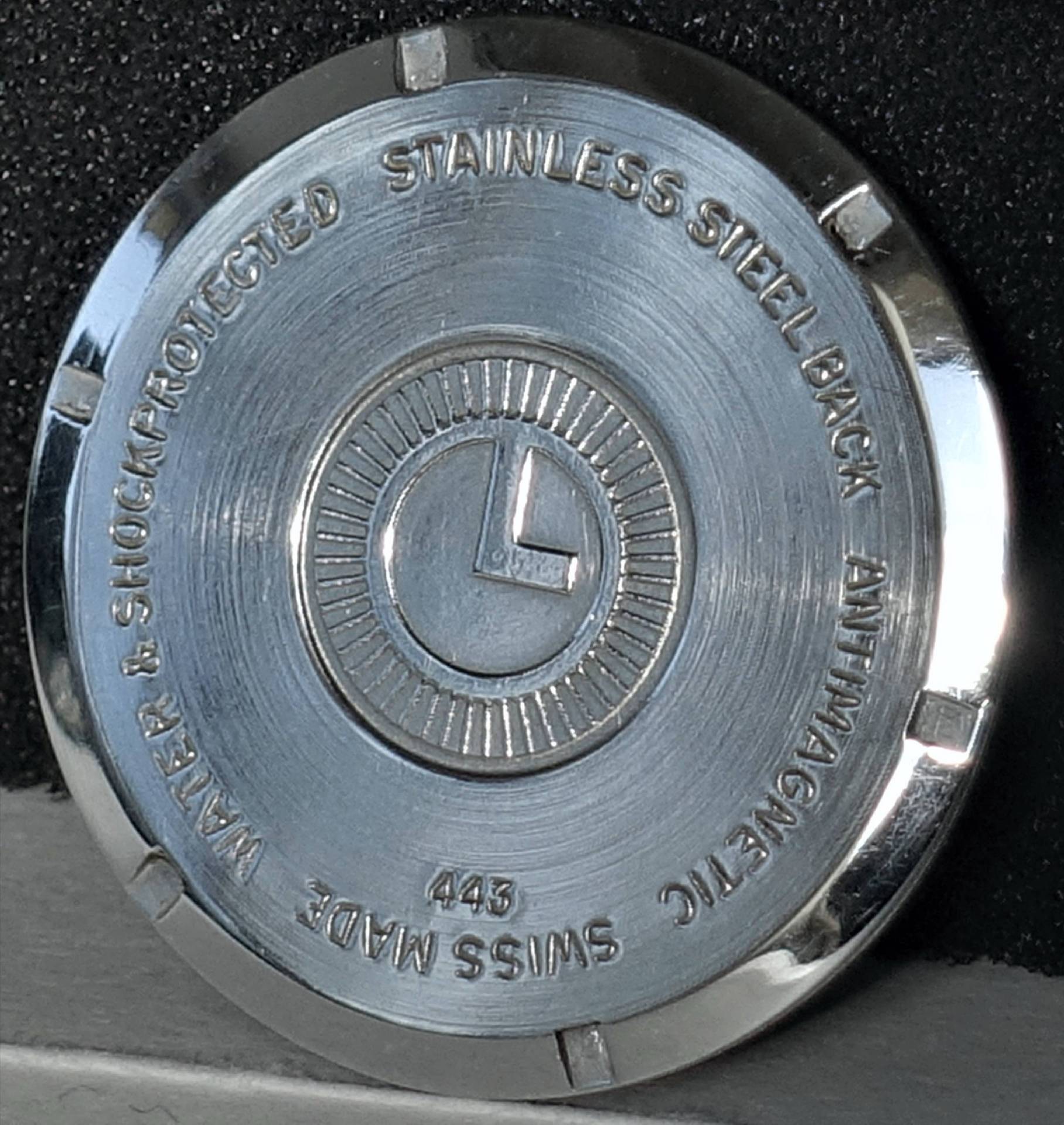 Silberfarbener runder Uhrboden mit Gravur und zentralem Logo.